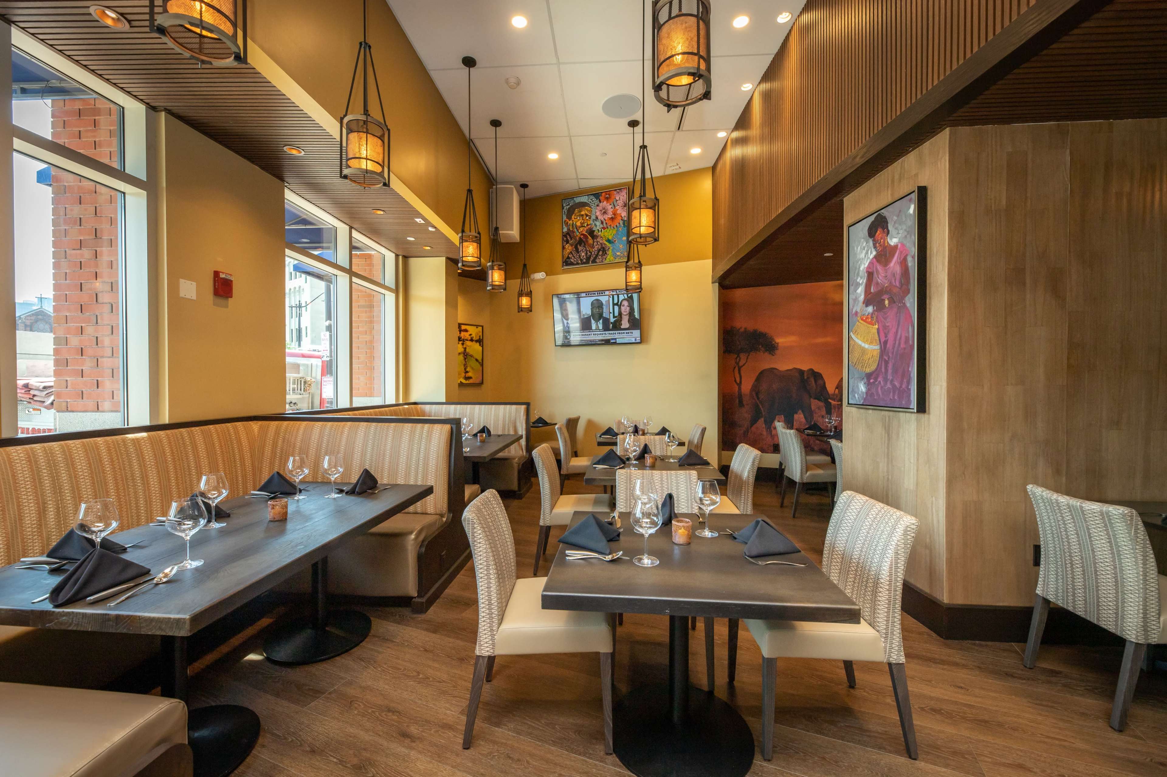 A modern restaurant interior with tables set for dining, featuring elegant lighting and decorative artwork on the walls.