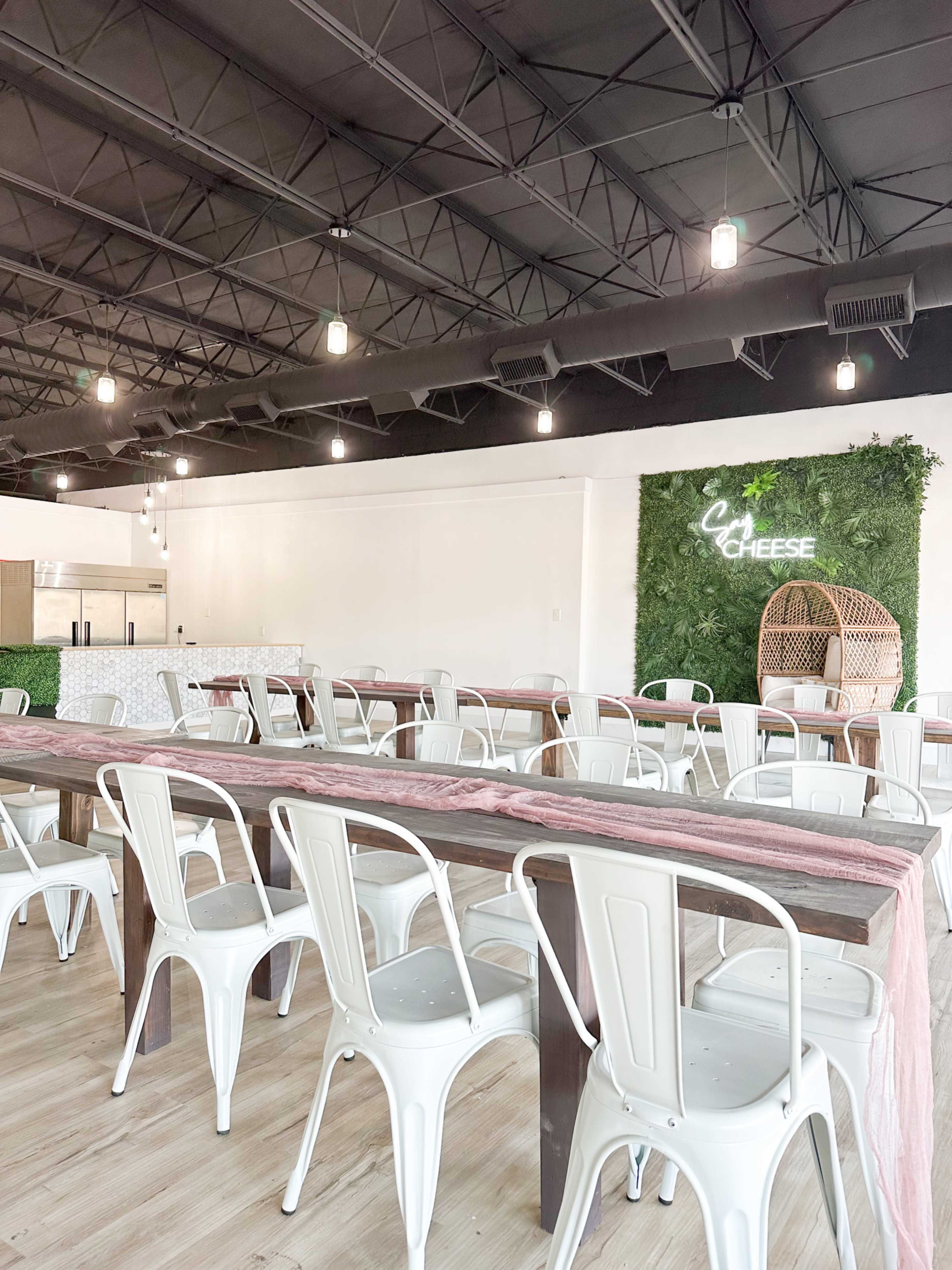 A spacious dining area with white metal chairs arranged around wooden tables and greenery on the wall.