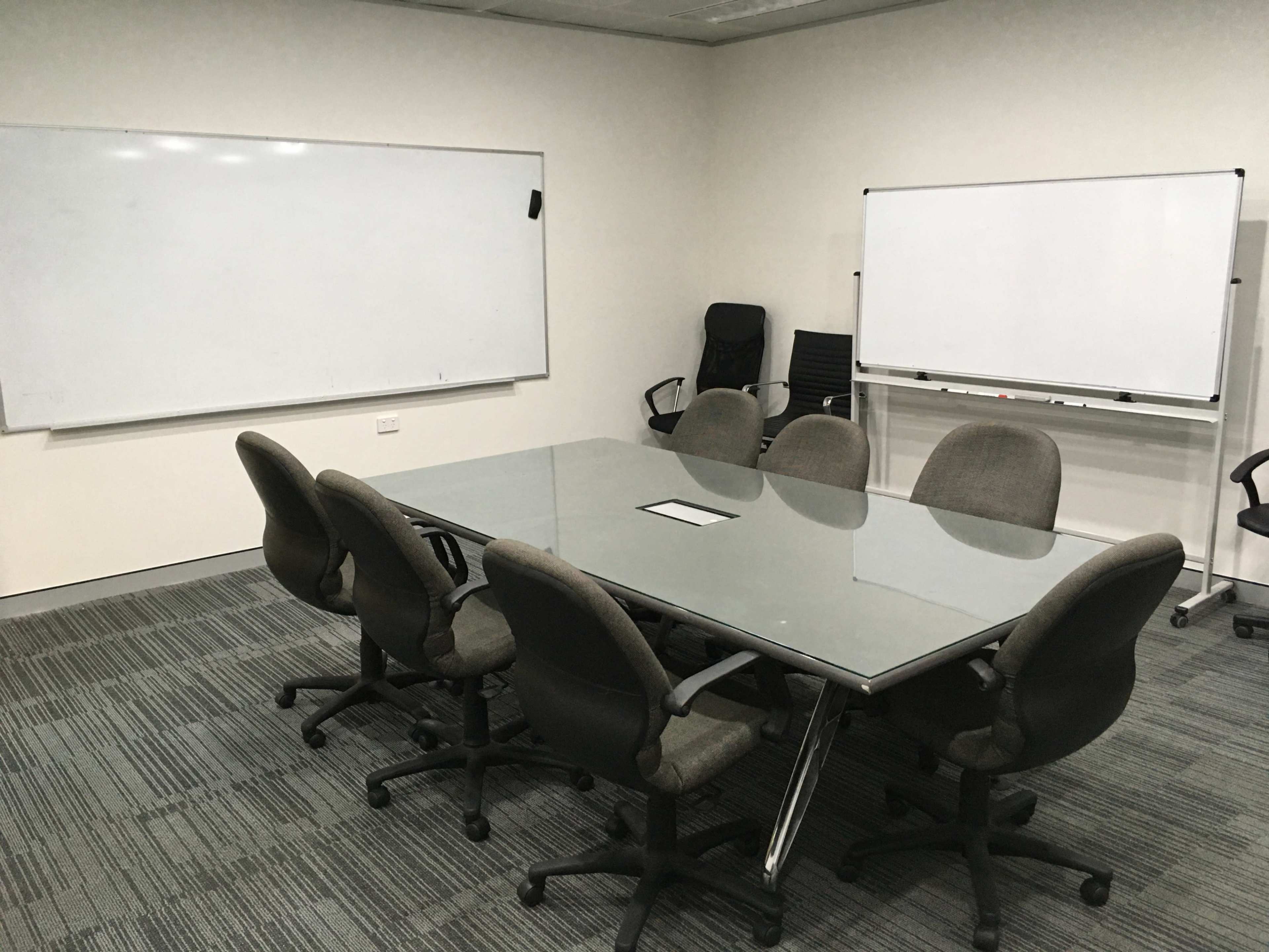 A glass-topped conference table surrounded by several office chairs in a meeting room with whiteboards on the walls.