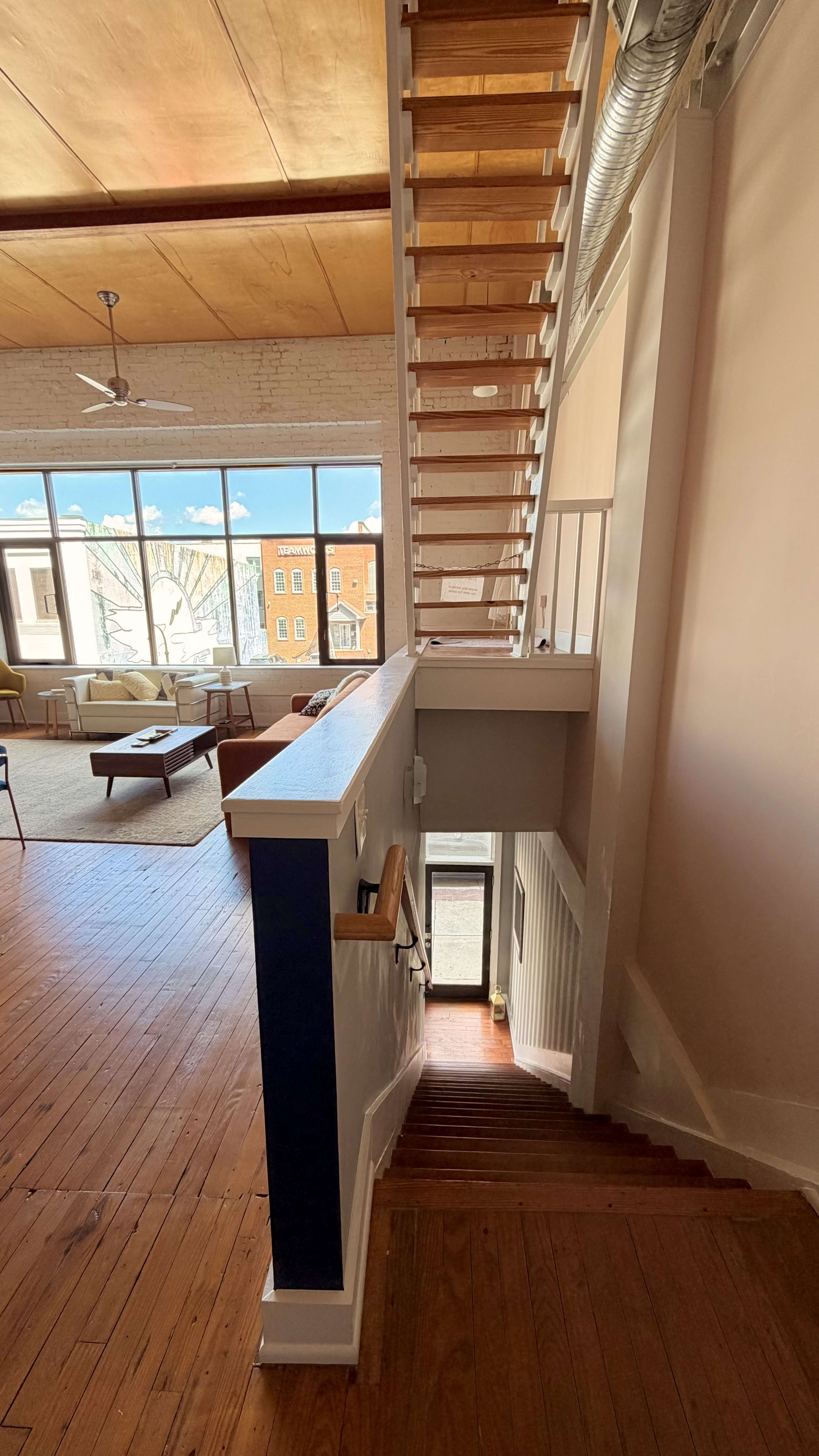 A wooden staircase leads upstairs within a spacious, light-filled interior adorned with large windows.