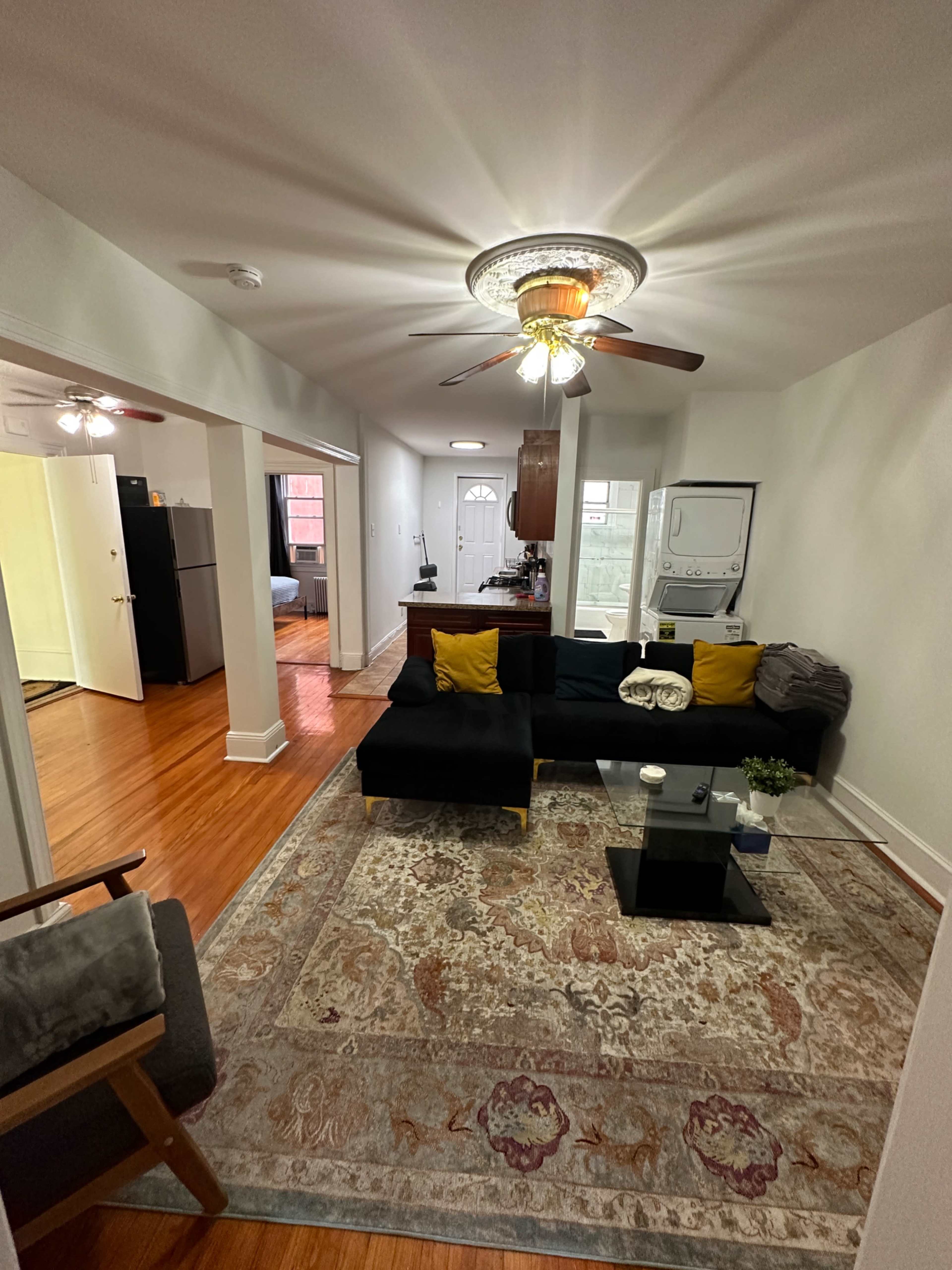 A living room with a sofa, coffee table, and an area rug, leading to a kitchen visible in the background.