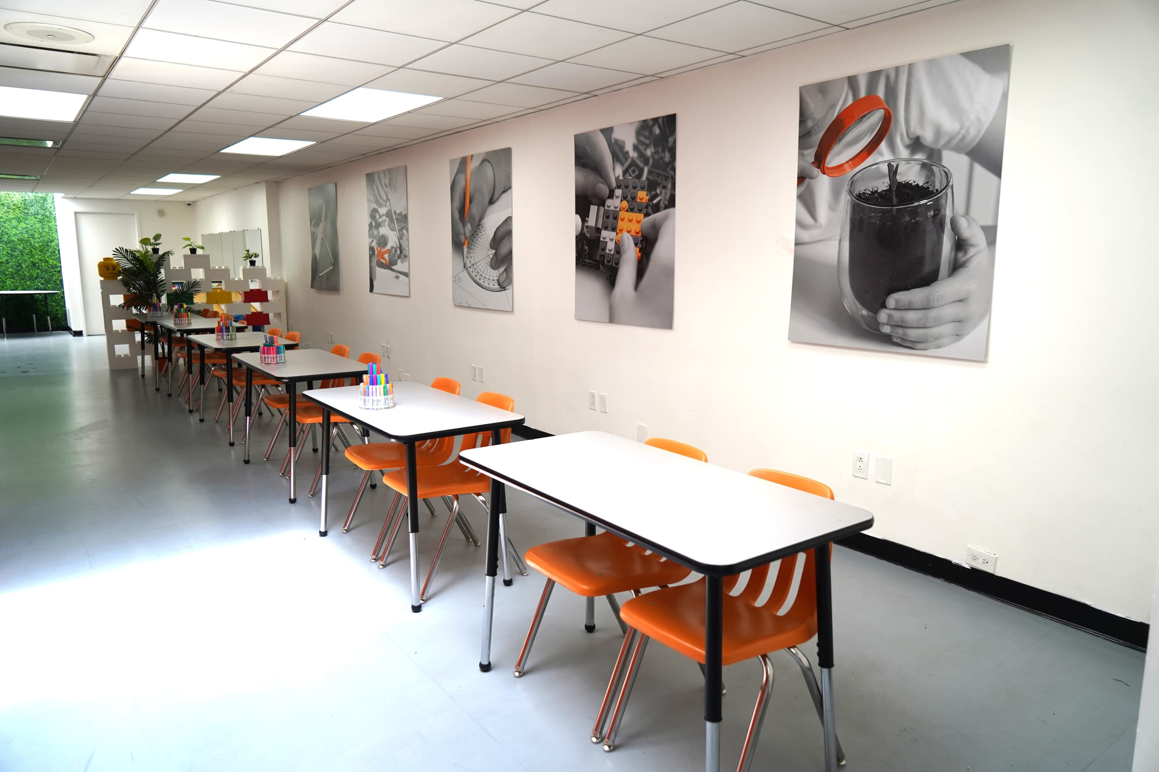 A long room features multiple tables with orange chairs, adorned with black and white photographs on the walls.