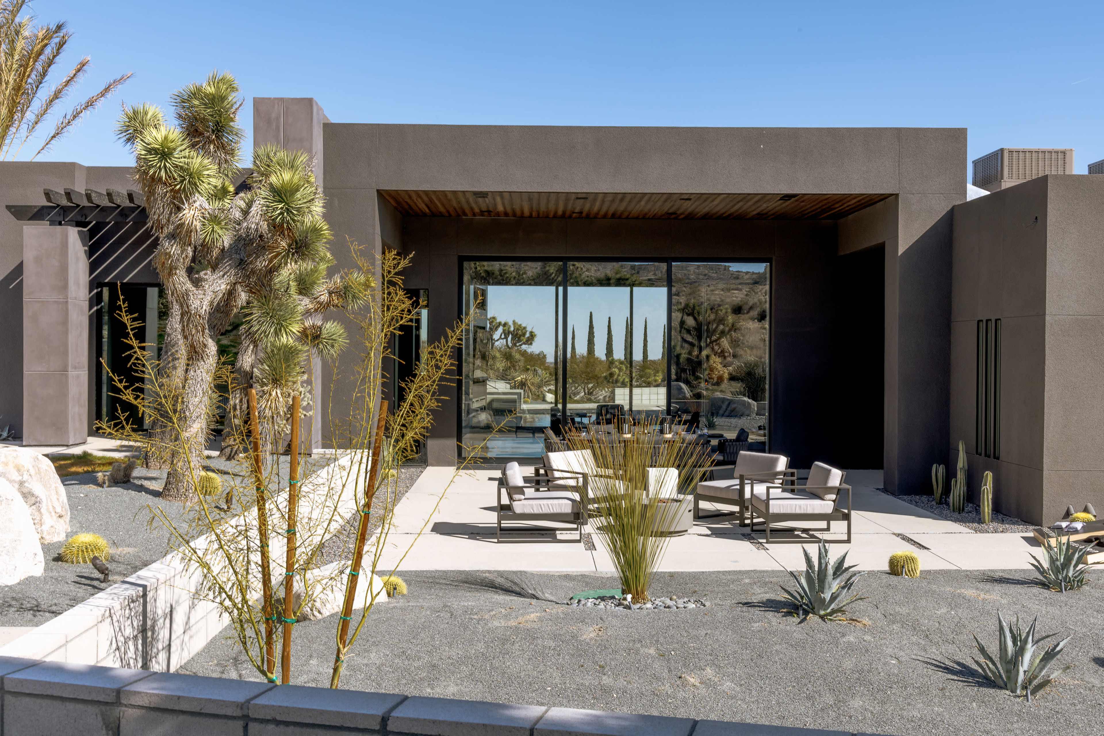 A modern house features a large glass patio door opening to a landscaped area with desert plants and seating.