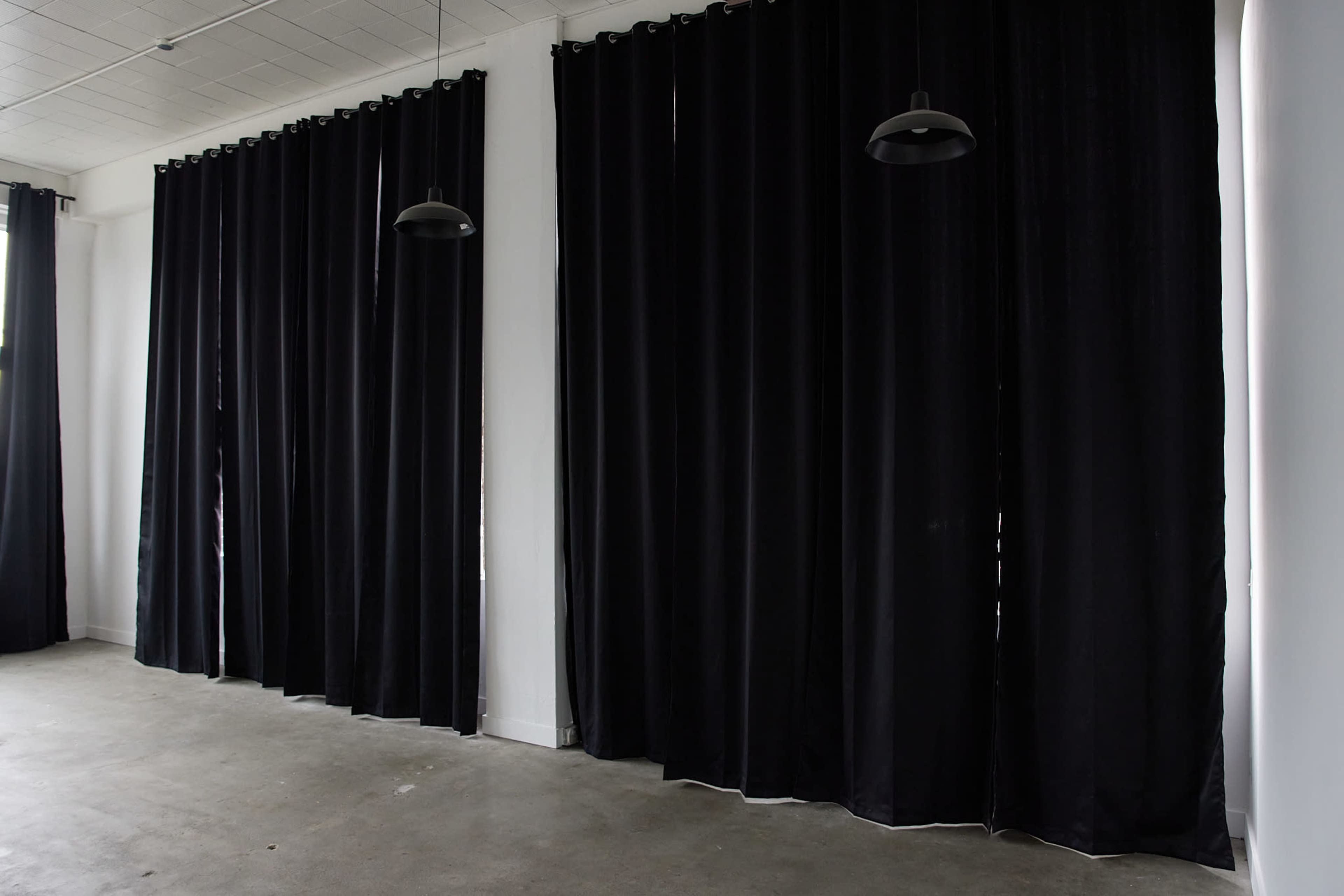 The image shows a room with high ceilings featuring long black curtains and several pendant lights hanging from the ceiling.