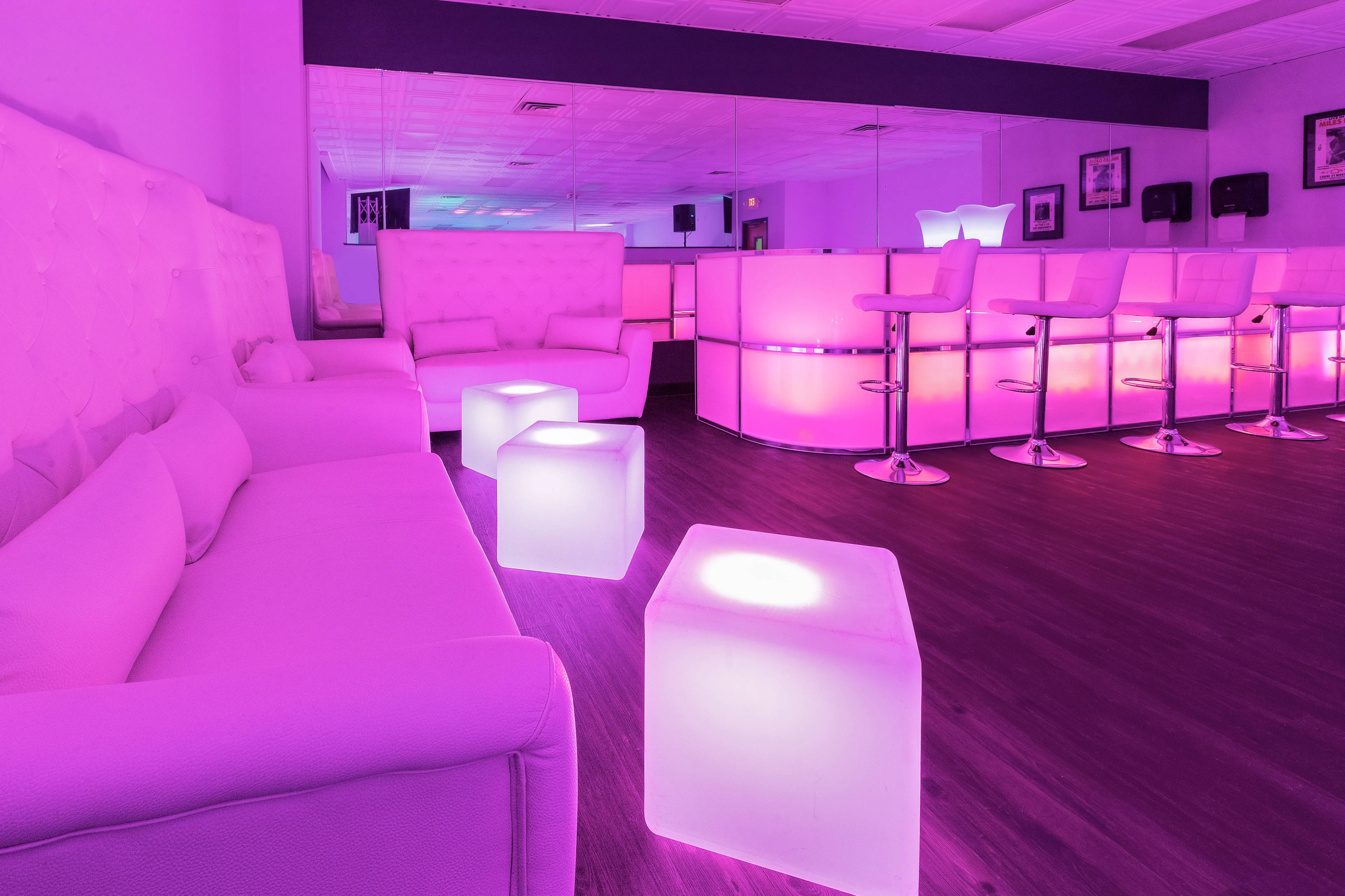 The image shows a modern lounge area with purple ambient lighting, featuring white furniture and glowing cube tables.