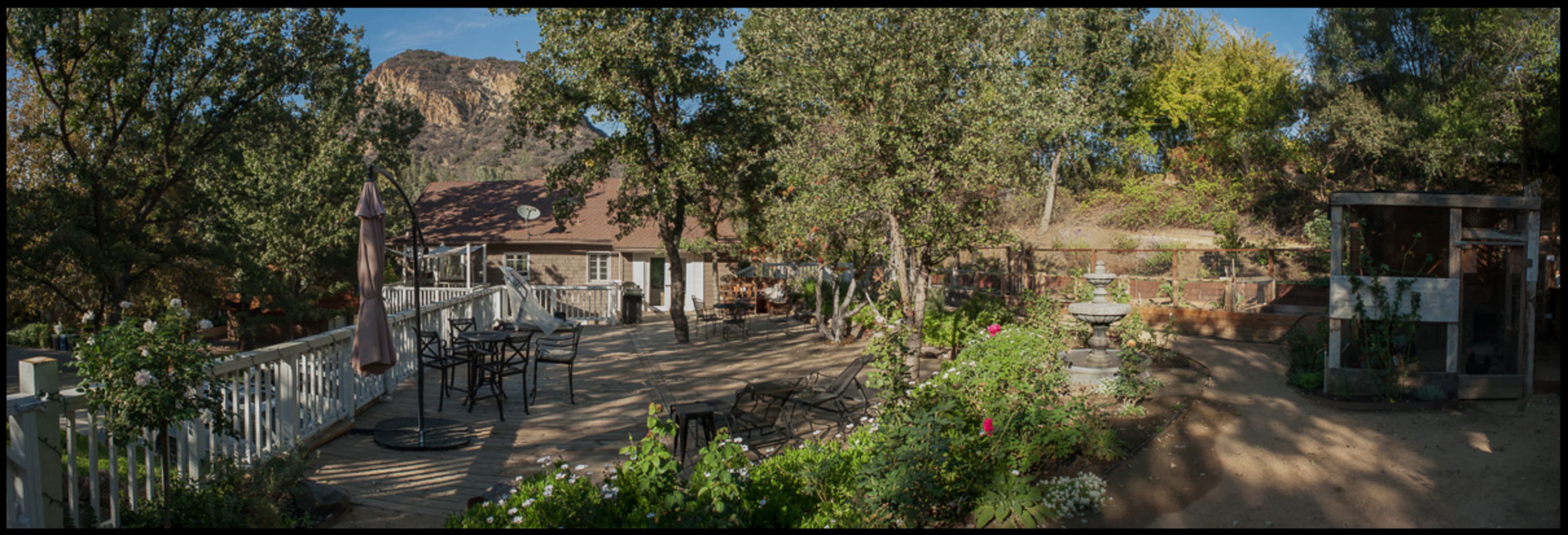 A wooden deck with outdoor seating and a garden area is surrounded by trees and overlooks a rocky hillside.