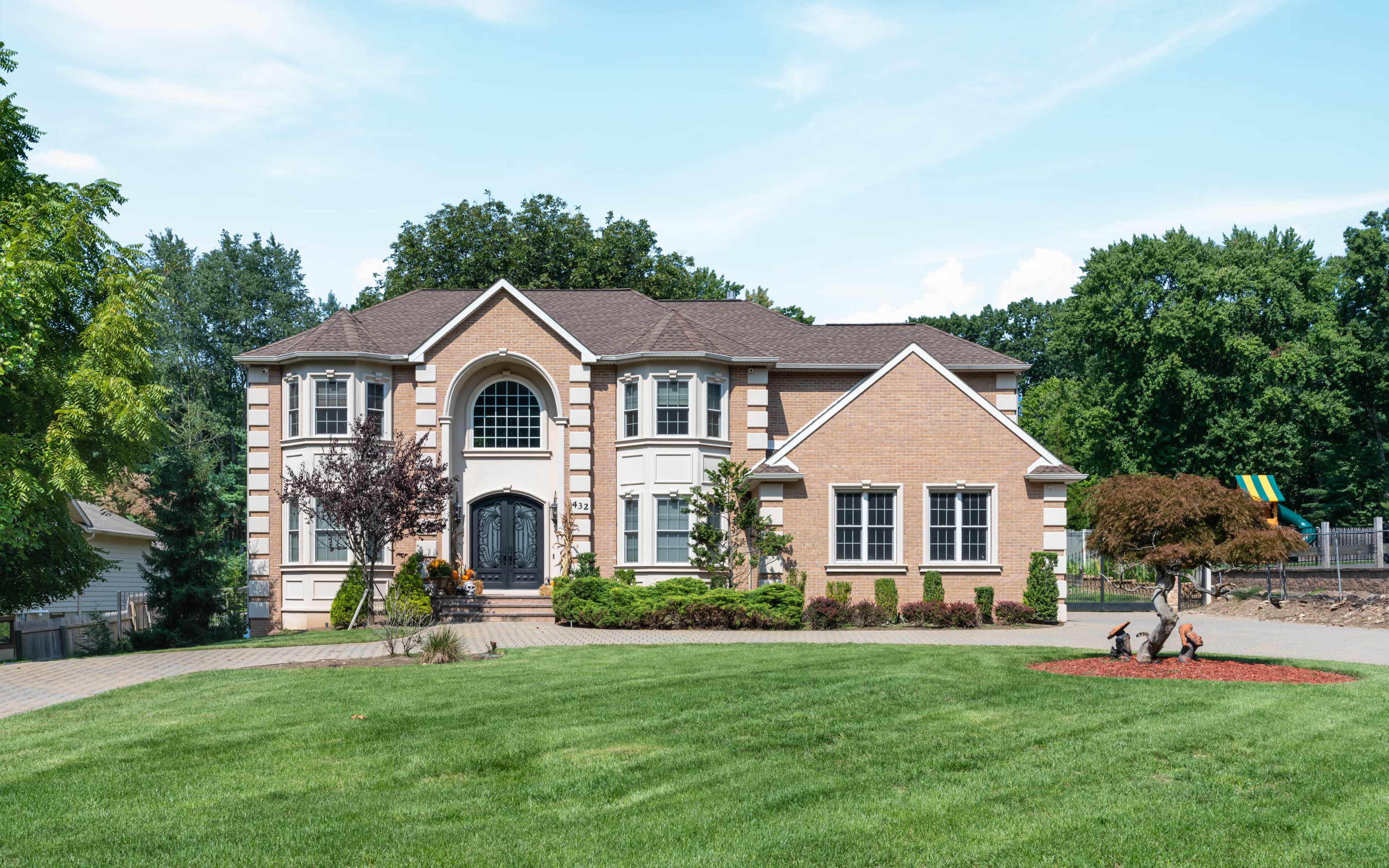 A large, two-story brick house with a manicured lawn and a paved driveway.