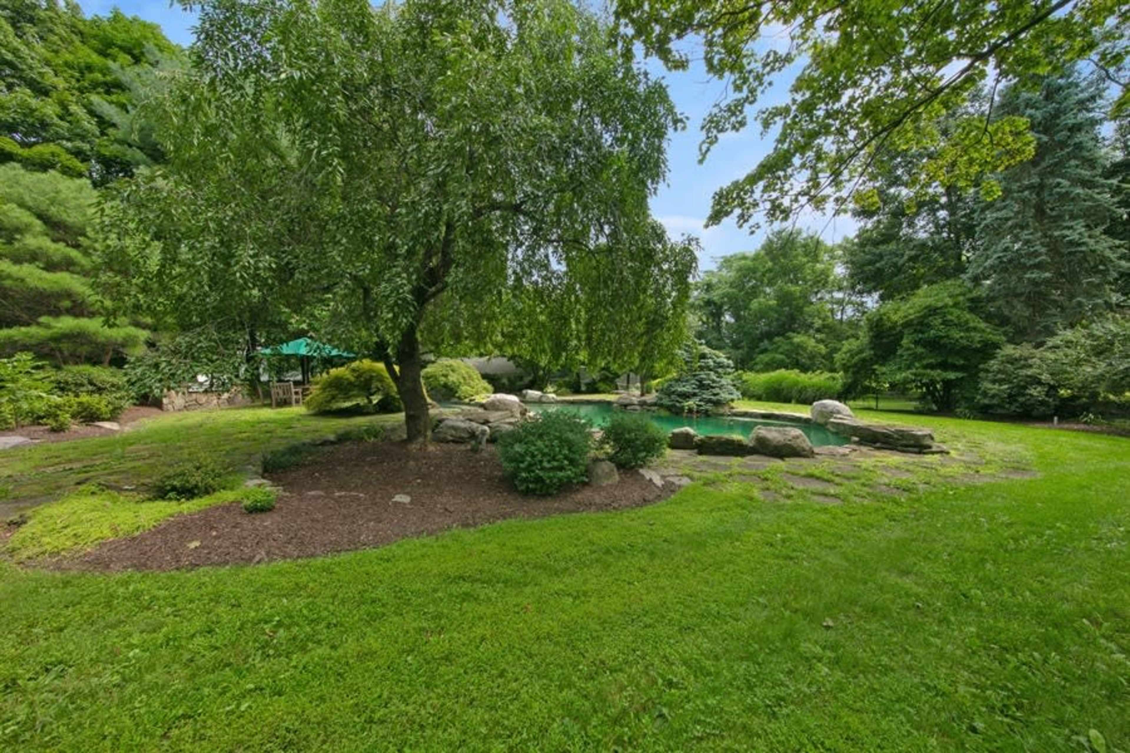 A spacious garden features a large tree, boulders, and a lush green lawn.