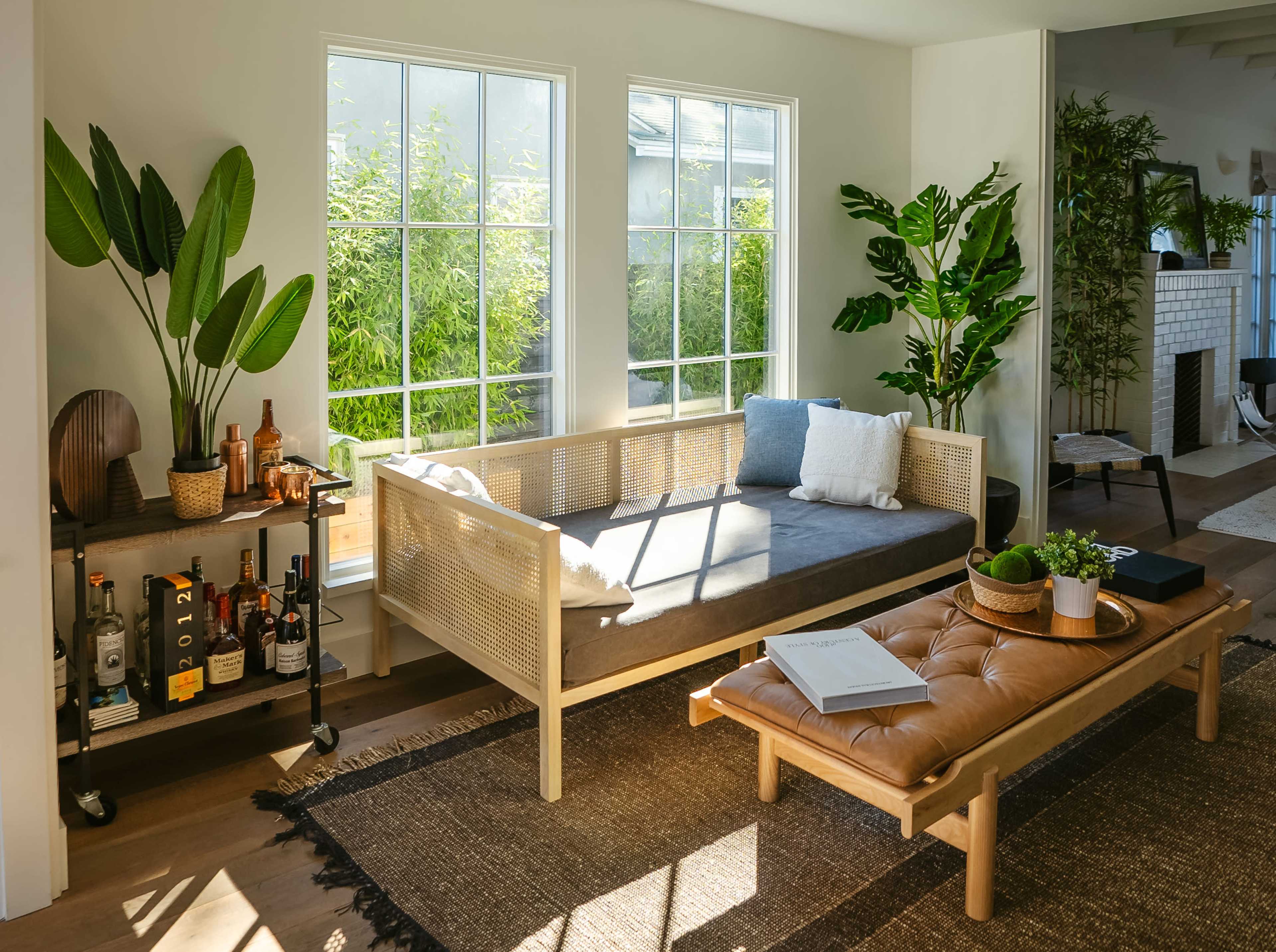 A bright, modern living room featuring a light-colored sofa, a wooden coffee table, and potted plants near large windows.