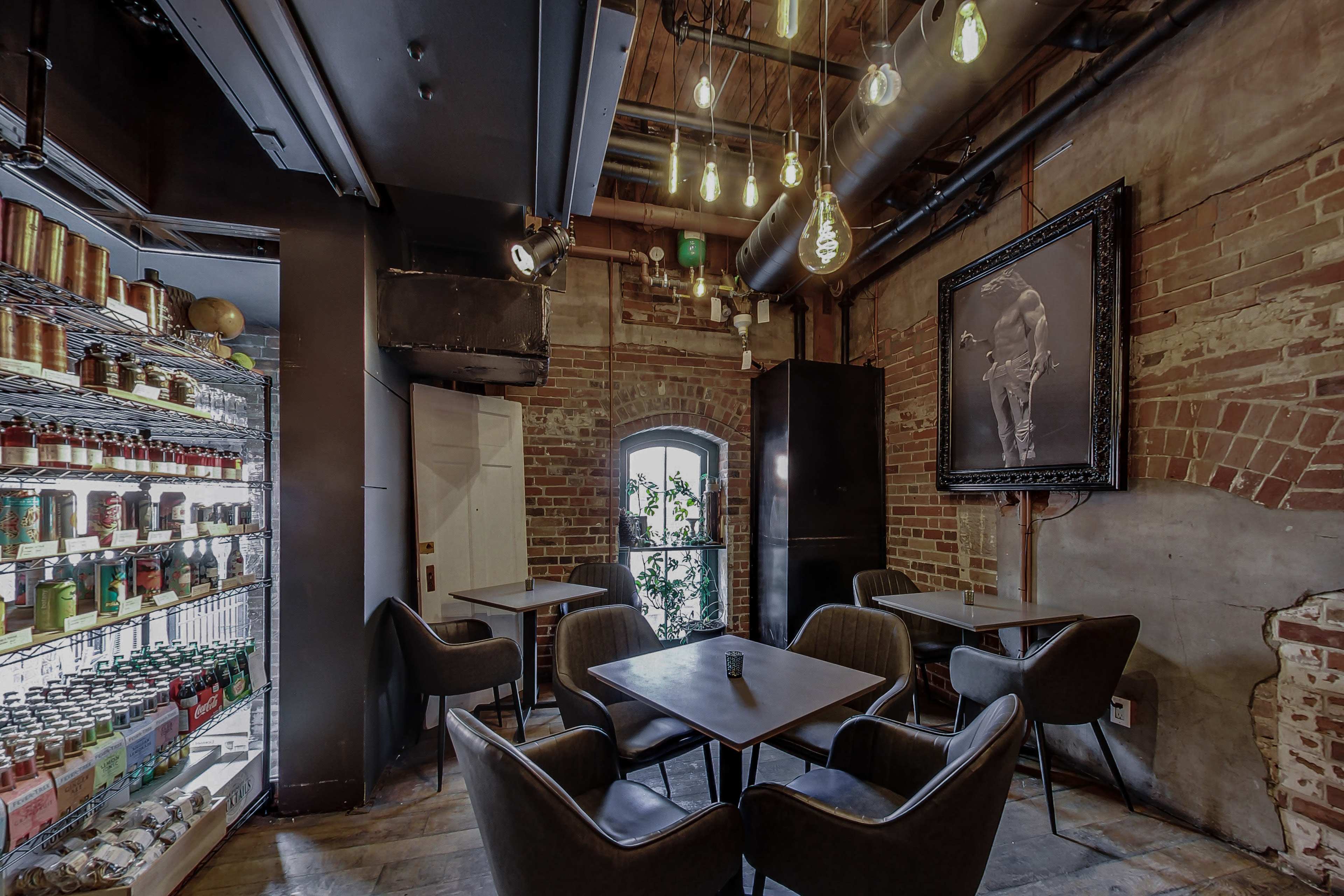 The image shows an interior of a modern café with brick walls, dark furniture, and a display of beverages in a glass refrigerator.