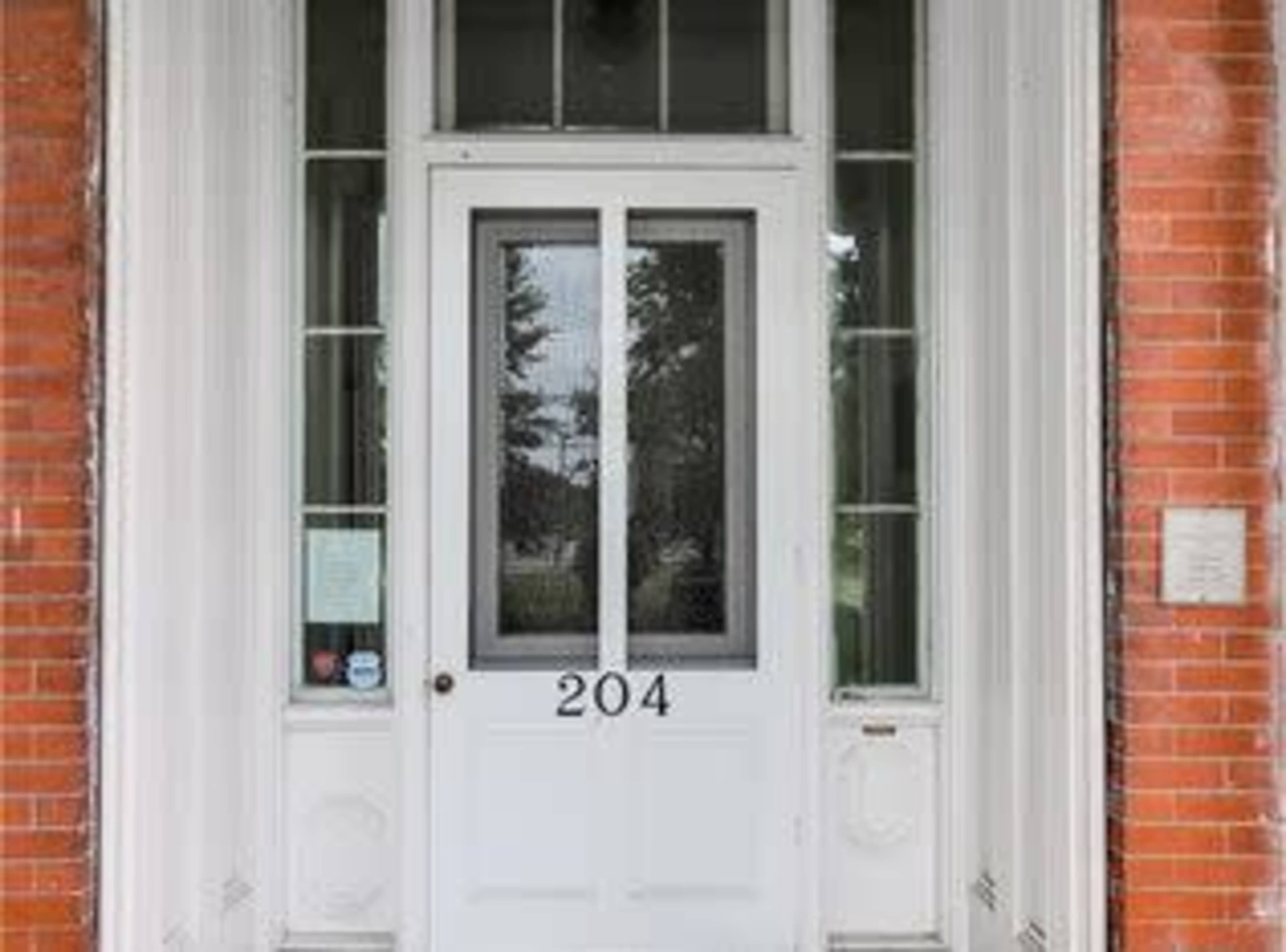 A white front door with the number "204" displayed prominently, framed by large windows and a brick facade.