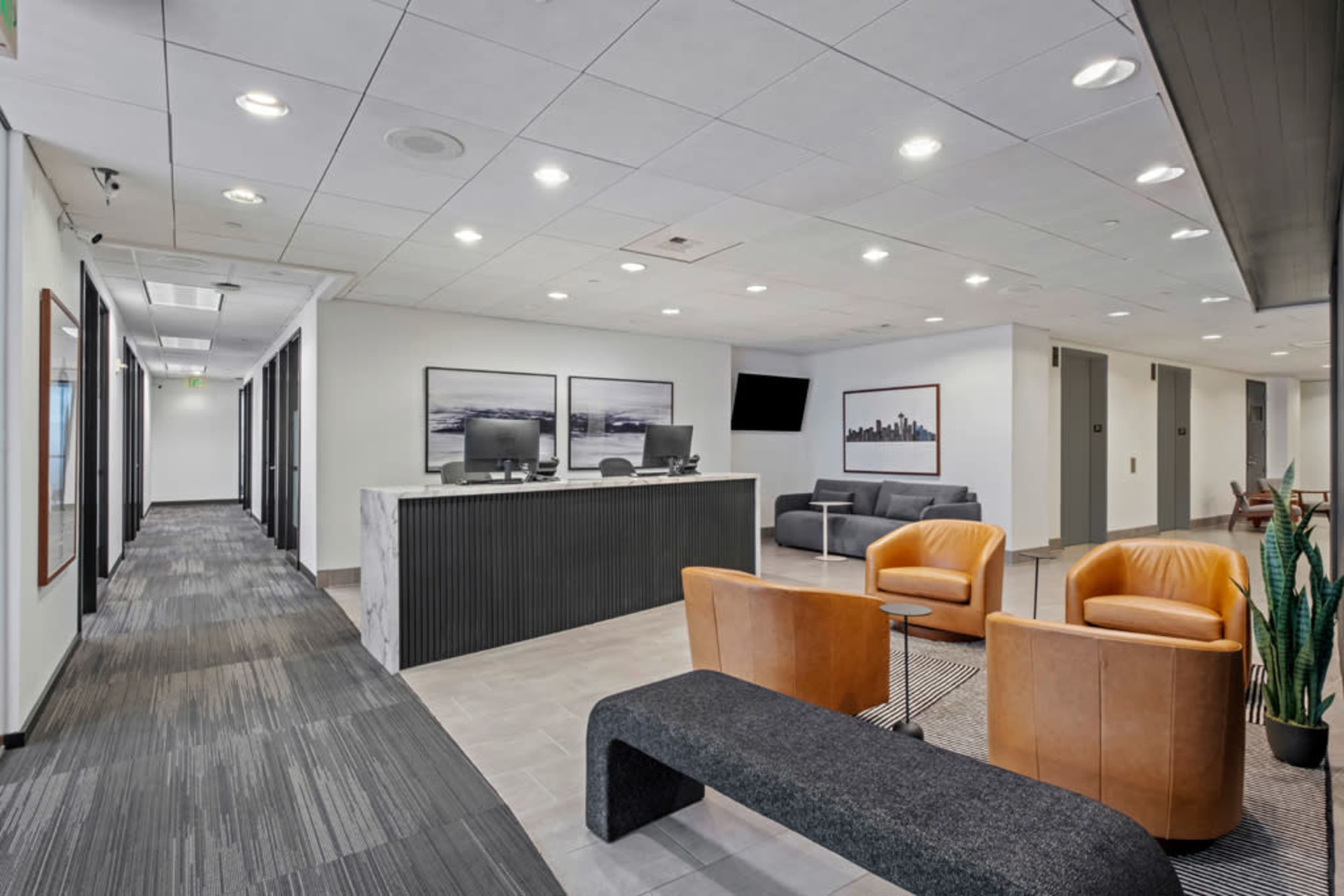 The image shows a modern office lobby with a reception area, seating, and a hallway leading to additional rooms.