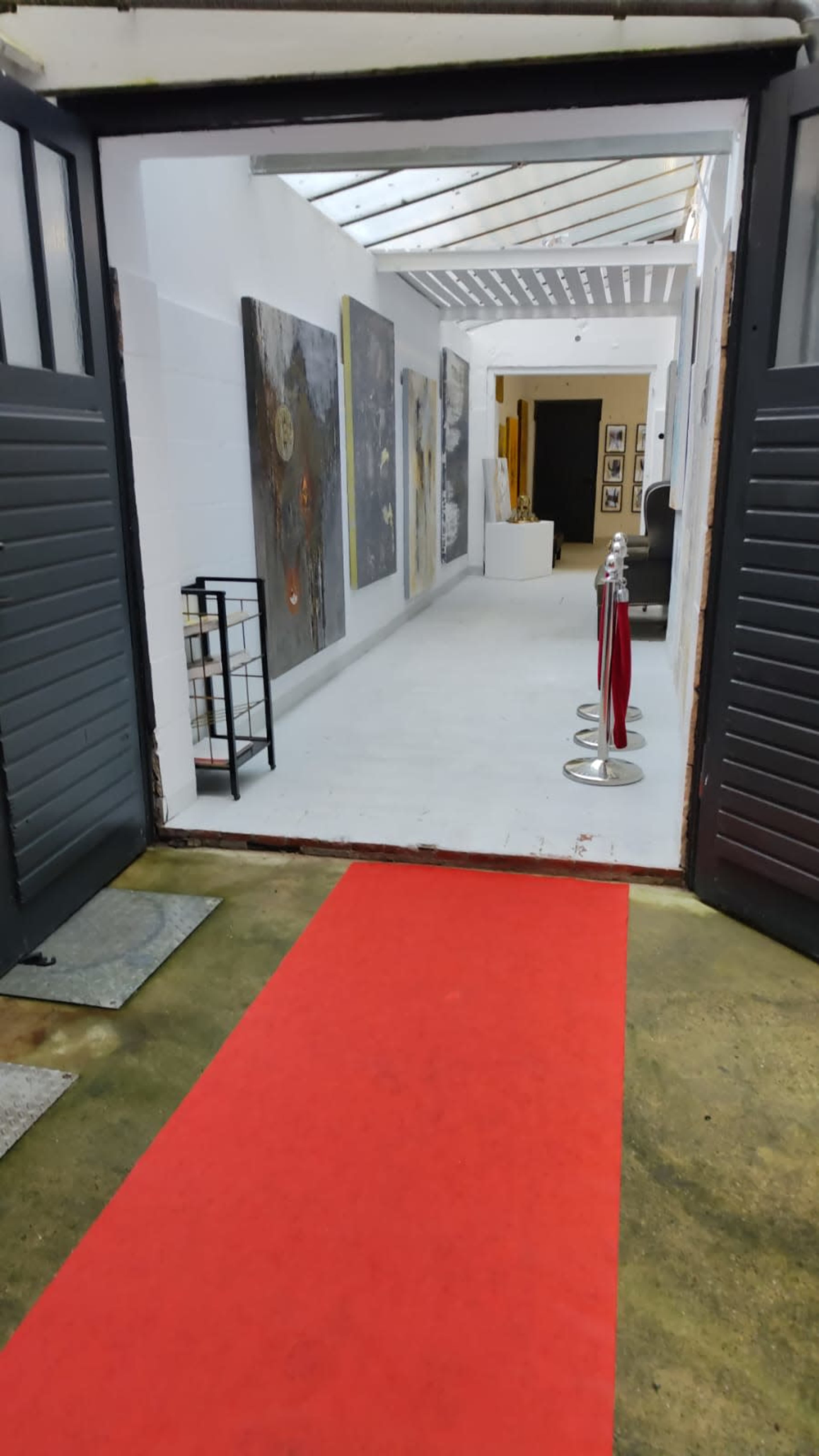 The image shows a red carpet leading into an art gallery with multiple paintings displayed on the walls.