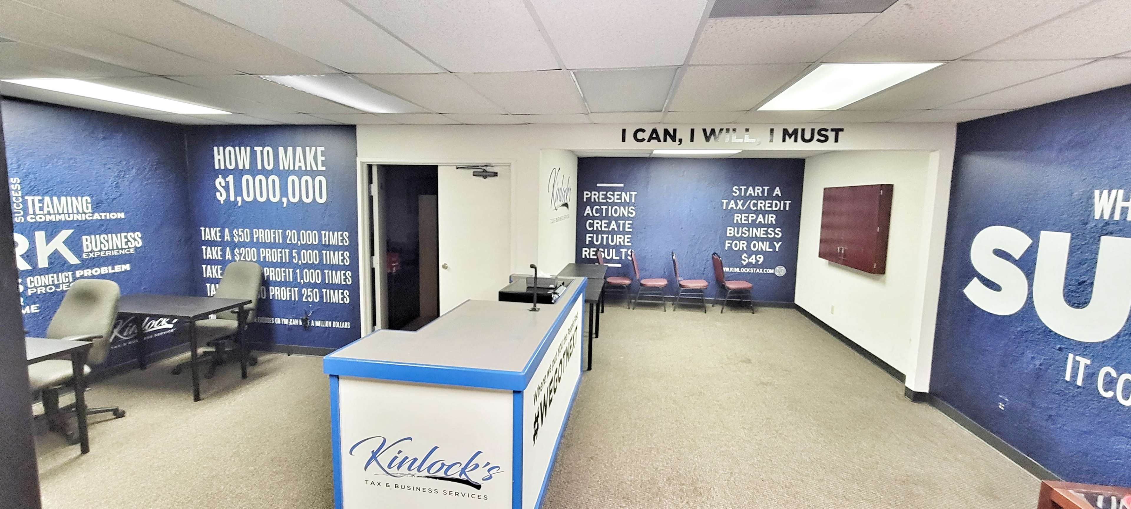 The image shows an office space with a reception area featuring a blue wall mural with motivational text, a service counter, and several chairs arranged for meetings.