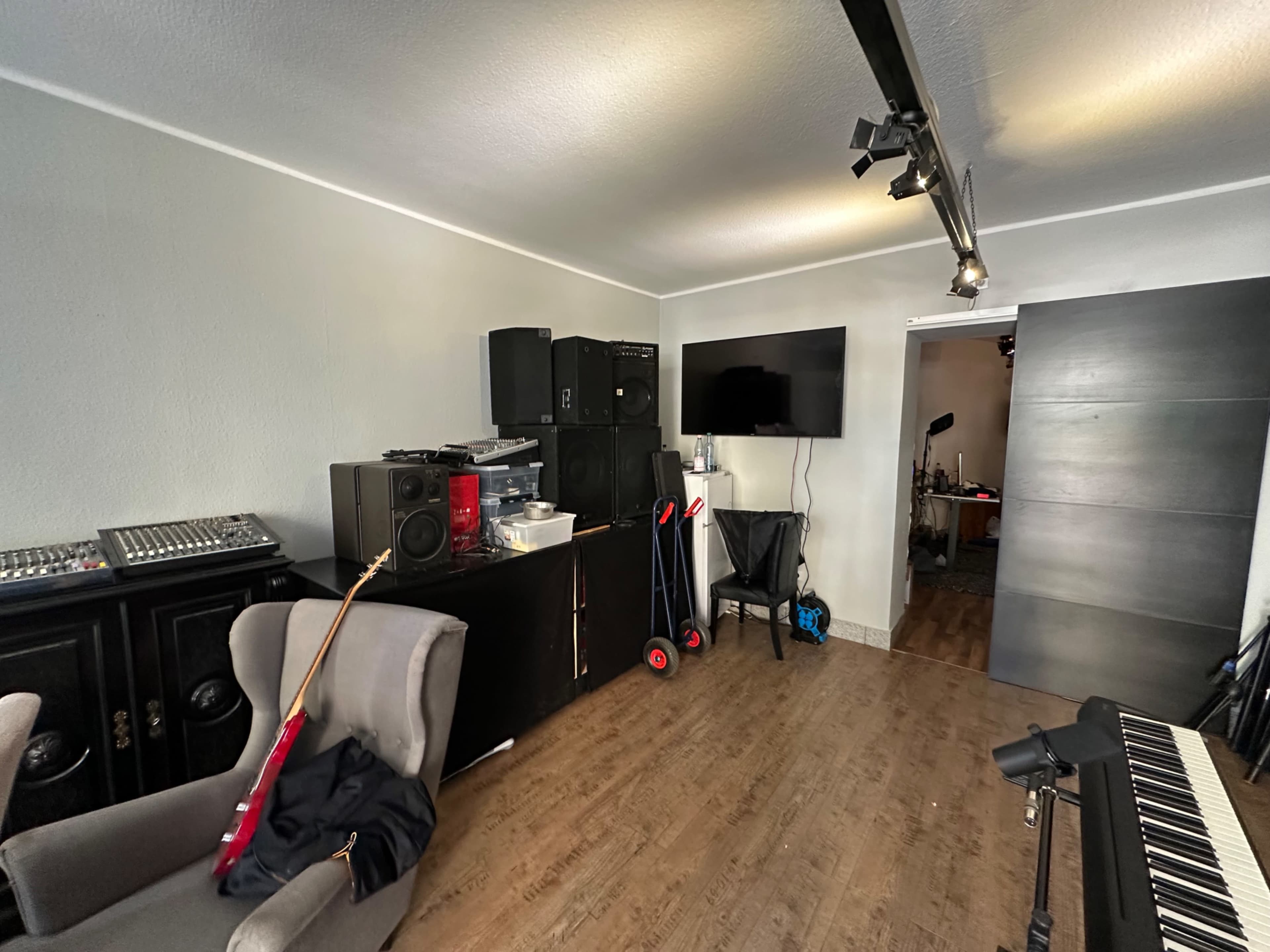 The image shows a music studio with a guitar, speakers, mixing equipment, and a large screen mounted on the wall.