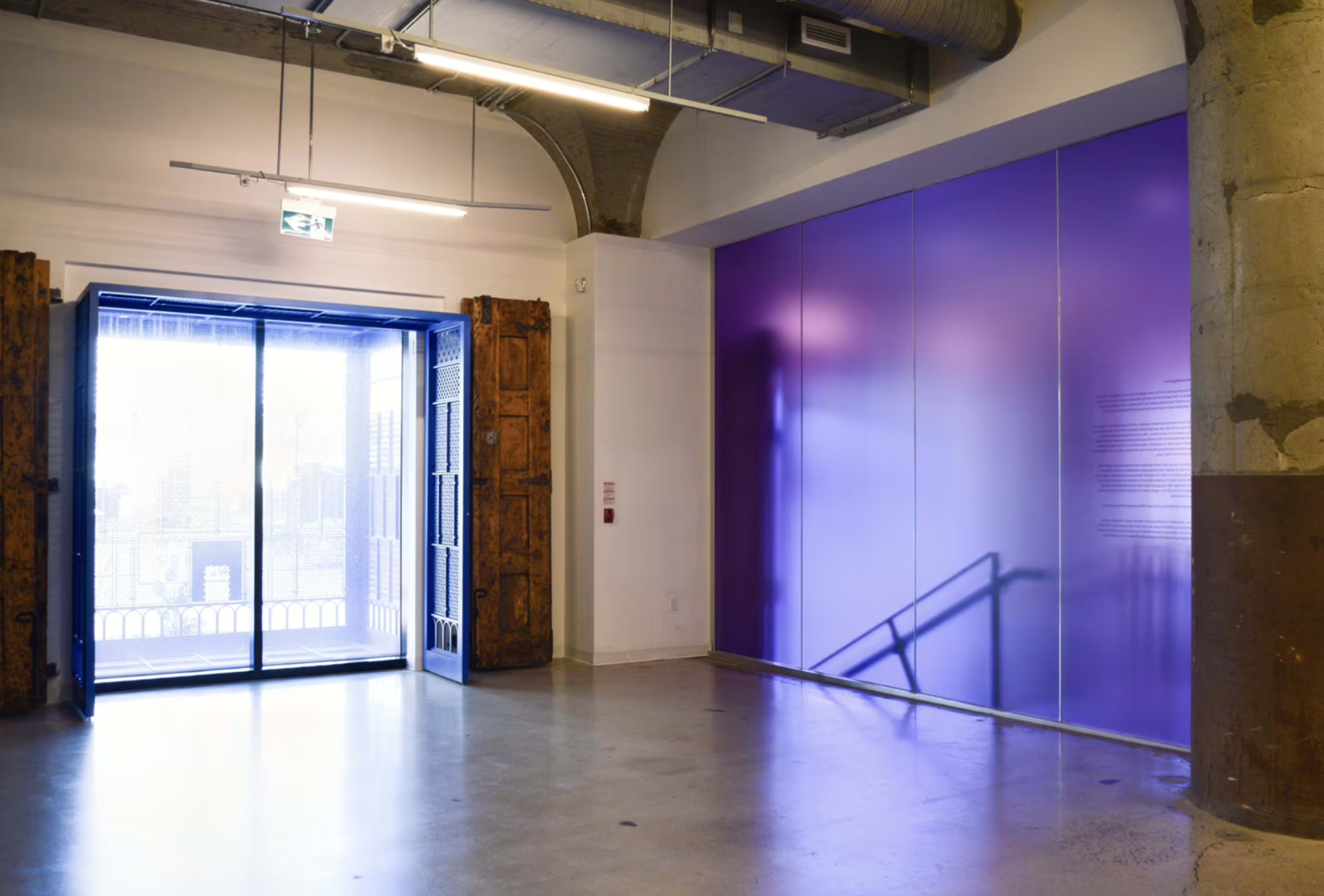 The image shows a spacious, brightly lit room with a large open door leading to an exterior view and a wall painted in a solid purple color.