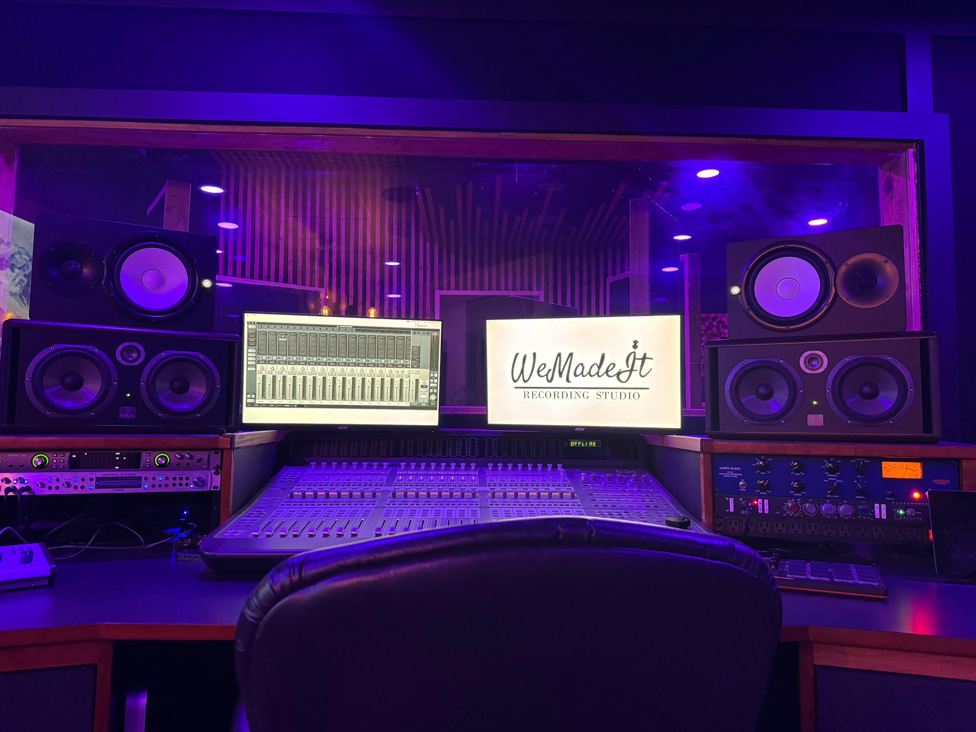 A recording studio is depicted, featuring a mixing console, two computer monitors, and large speakers against a backdrop of purple lighting.