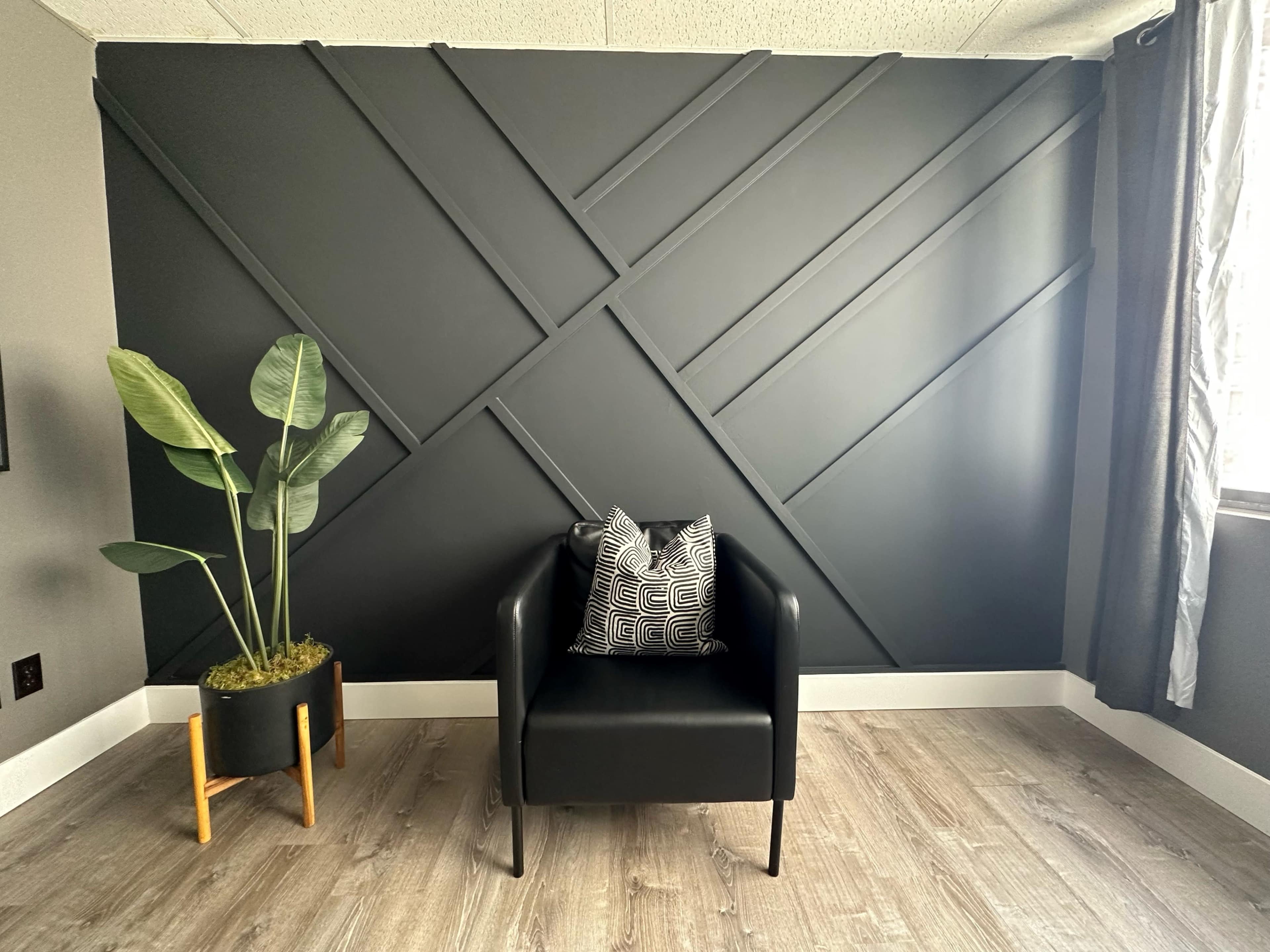 A black accent wall with diagonal wooden paneling, alongside a black armchair and a potted plant in a modern pot.