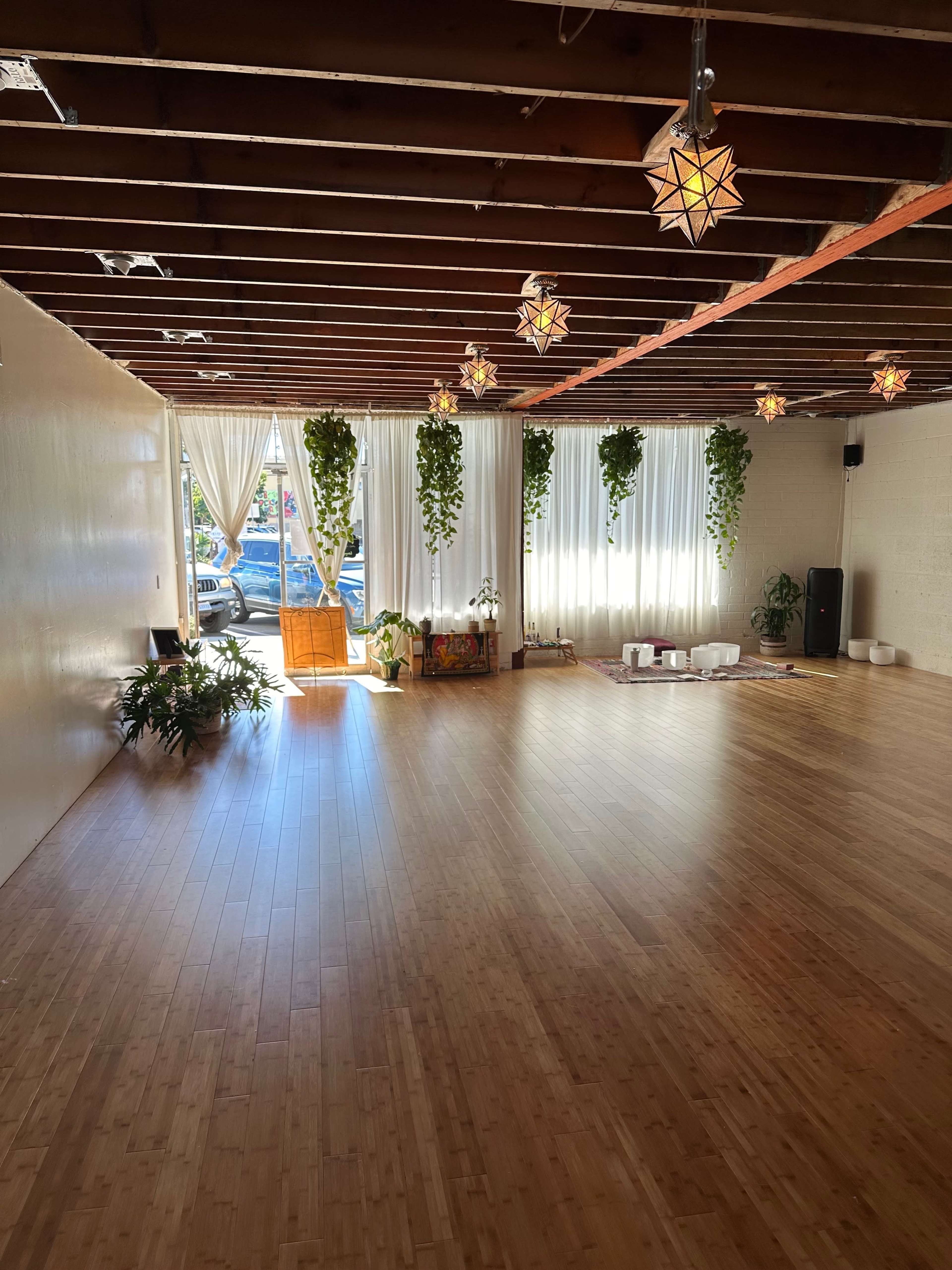 A spacious room with bamboo flooring, large windows draped in white curtains, and hanging plants, illuminated by star-shaped pendant lights.
