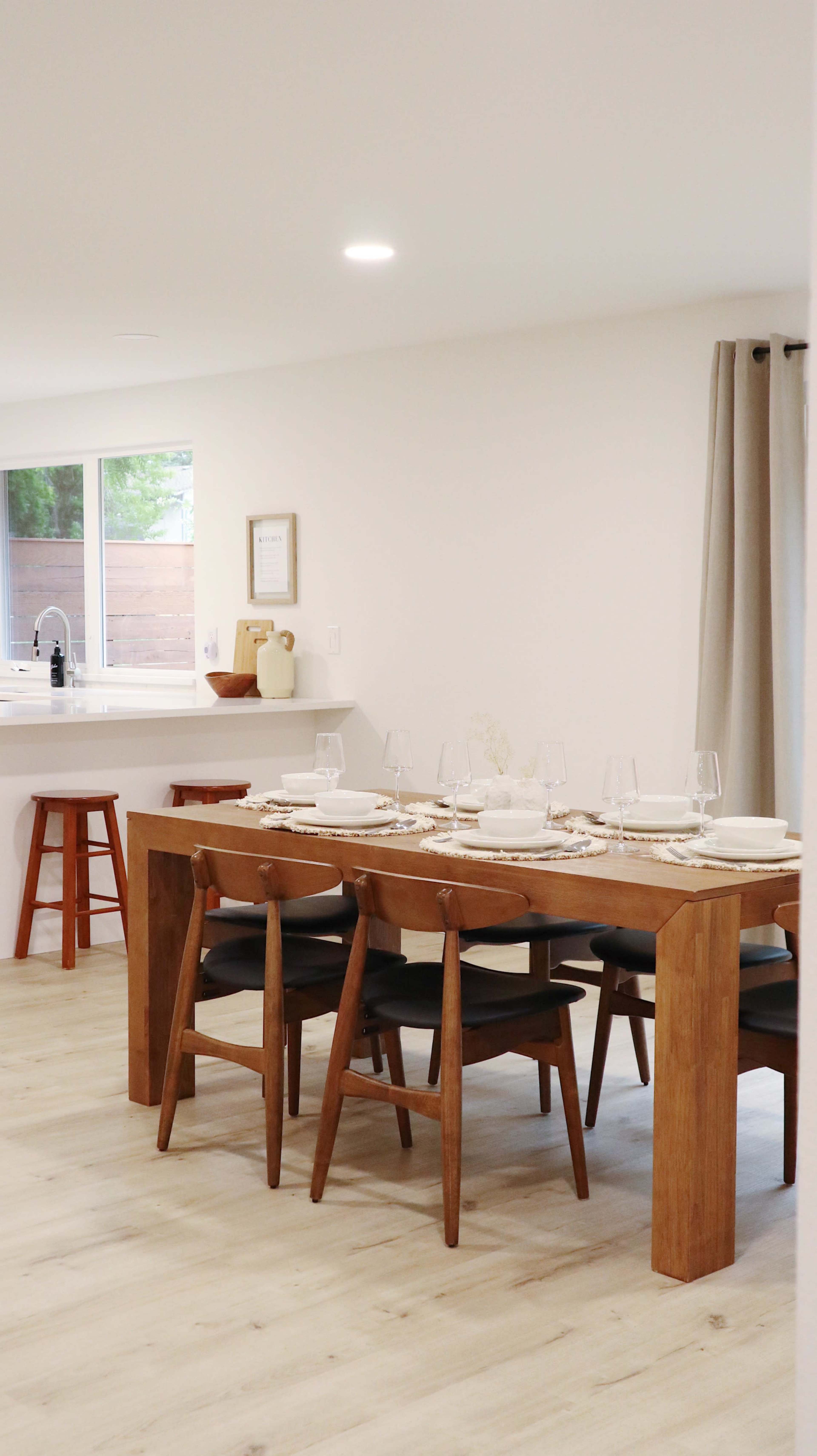 A modern dining area features a wooden table set for a meal with chairs and a window displaying a view of the outdoors.