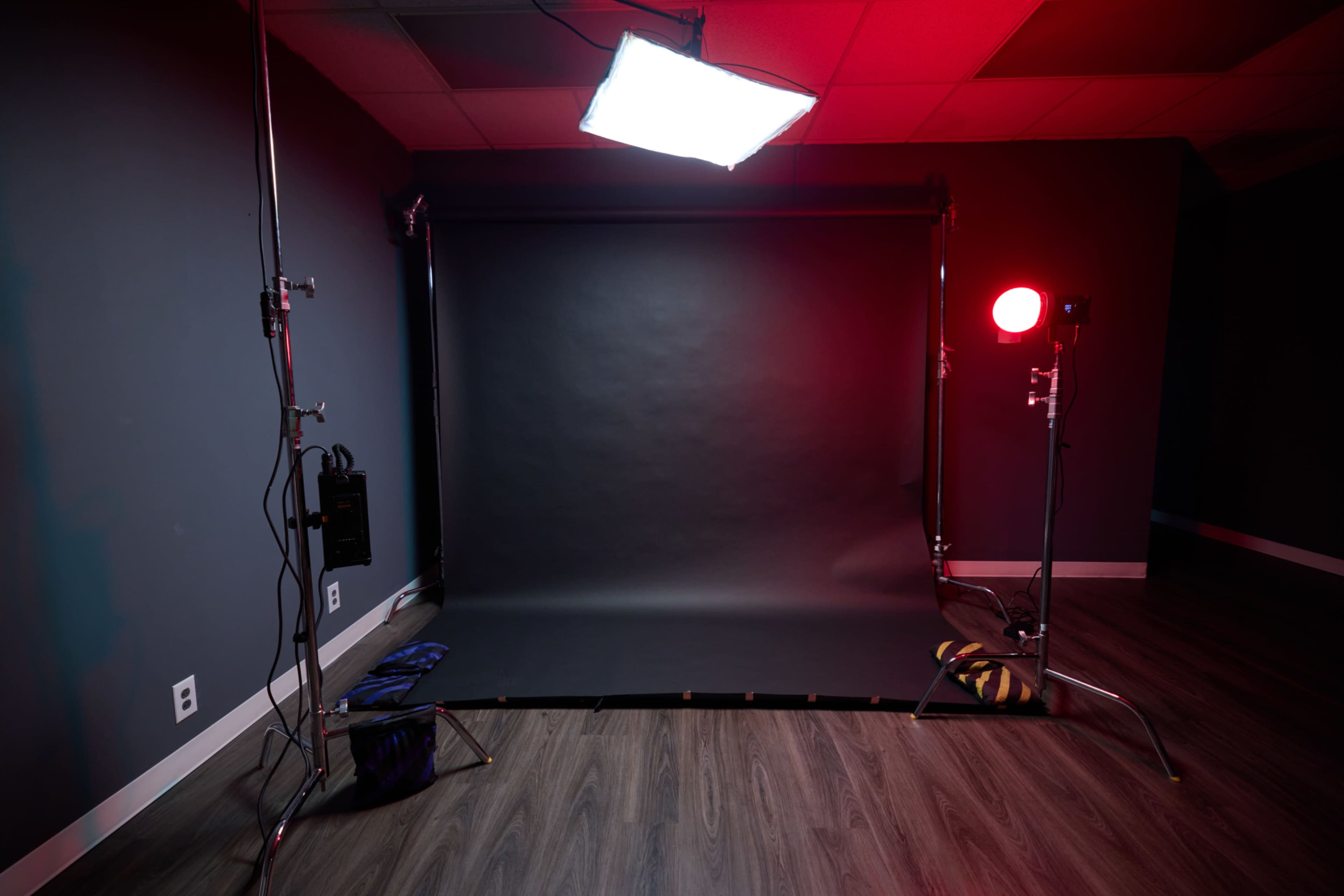 A photography studio setup features a black backdrop illuminated by a large softbox and a red light, with equipment stands on either side.