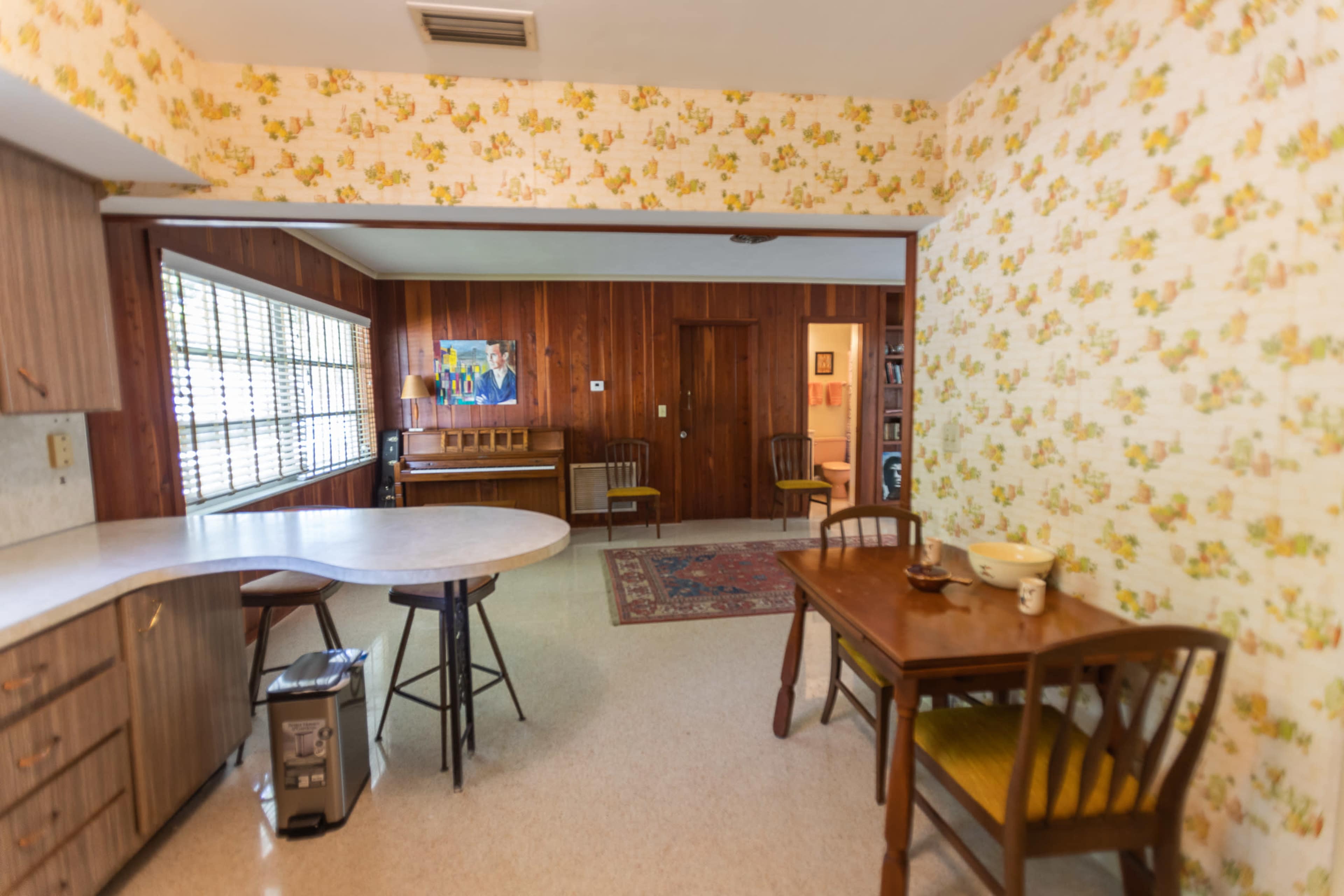 A kitchen and dining area display vintage decor and furniture, featuring a round table, chairs, and floral wallpaper.
