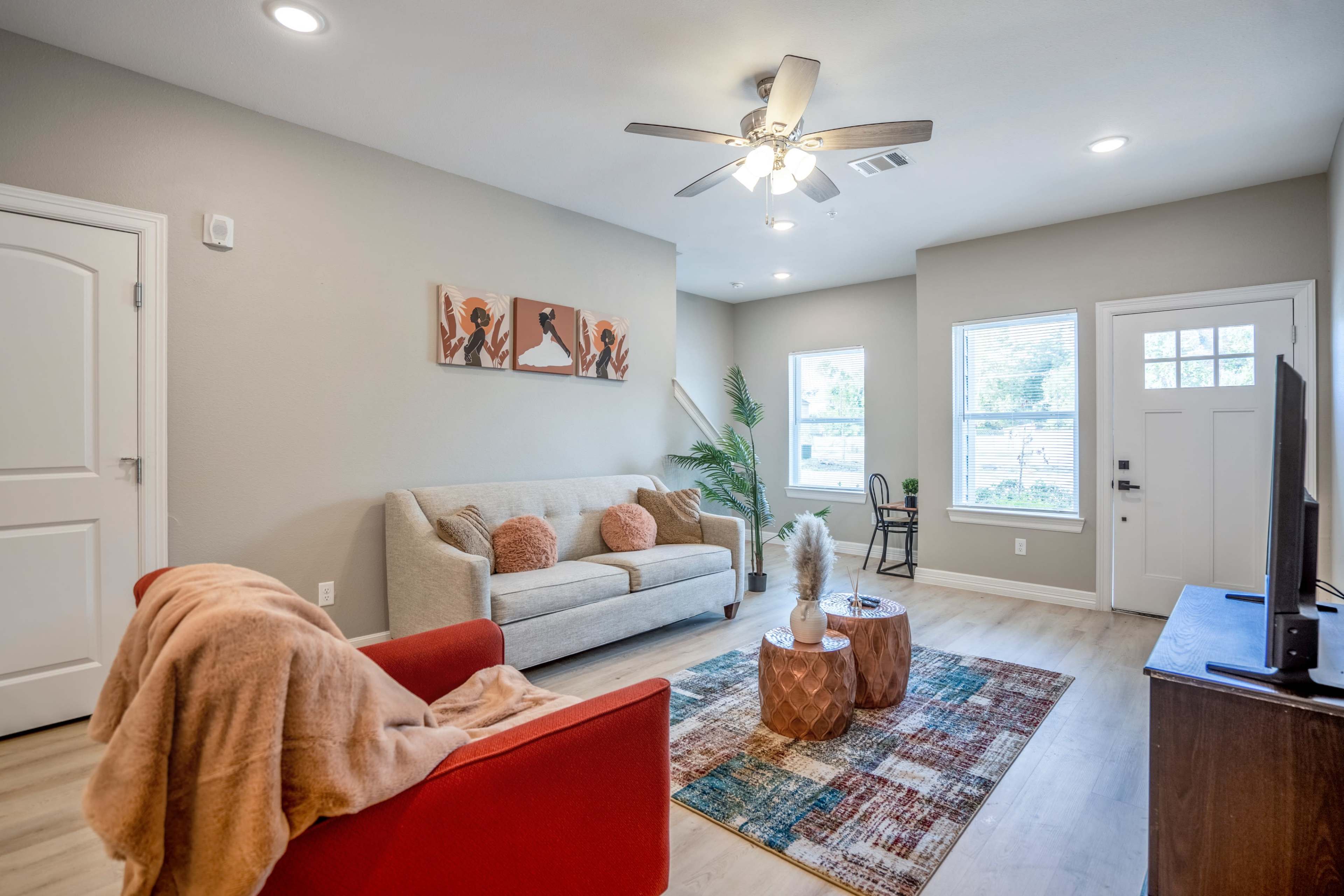 A modern living room features a light gray sofa, a red armchair, a decorative rug, and large windows that provide natural light.