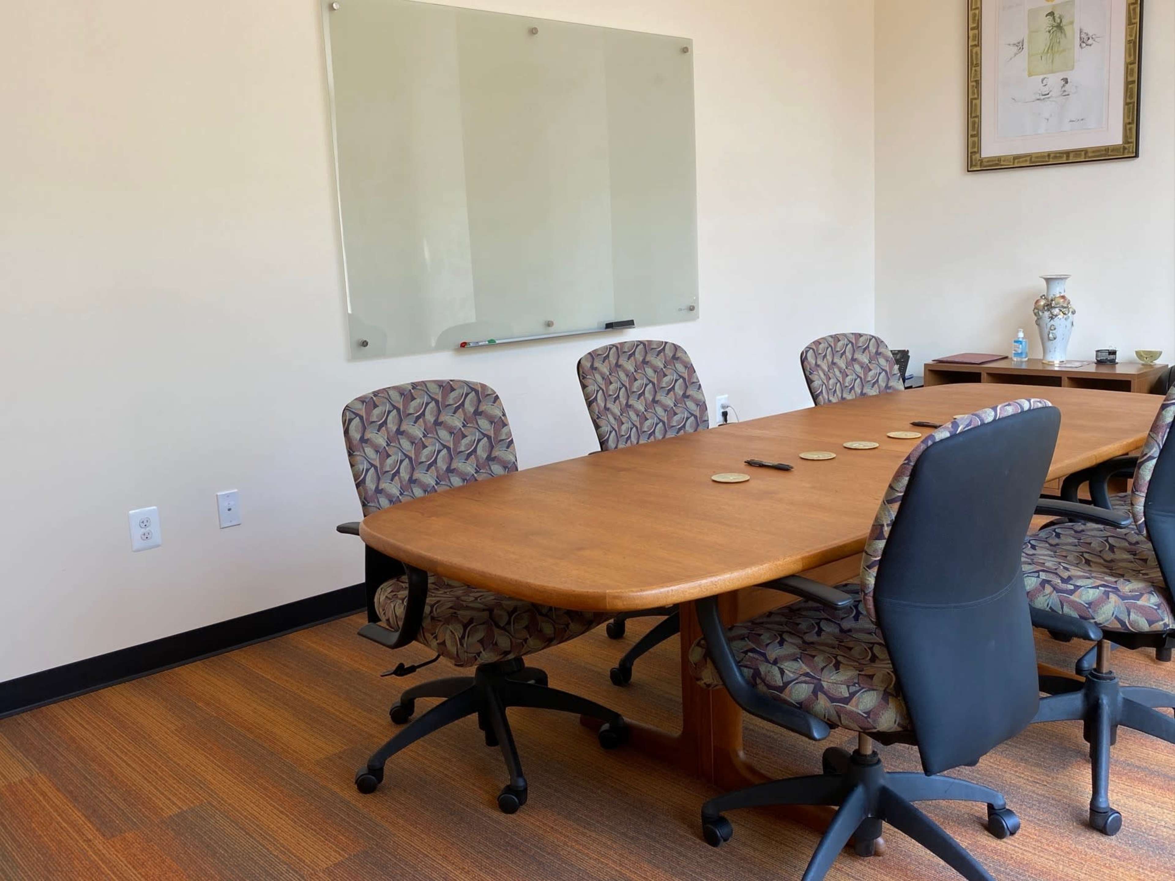 A conference room with a large wooden table, several patterned chairs, and a whiteboard mounted on the wall.