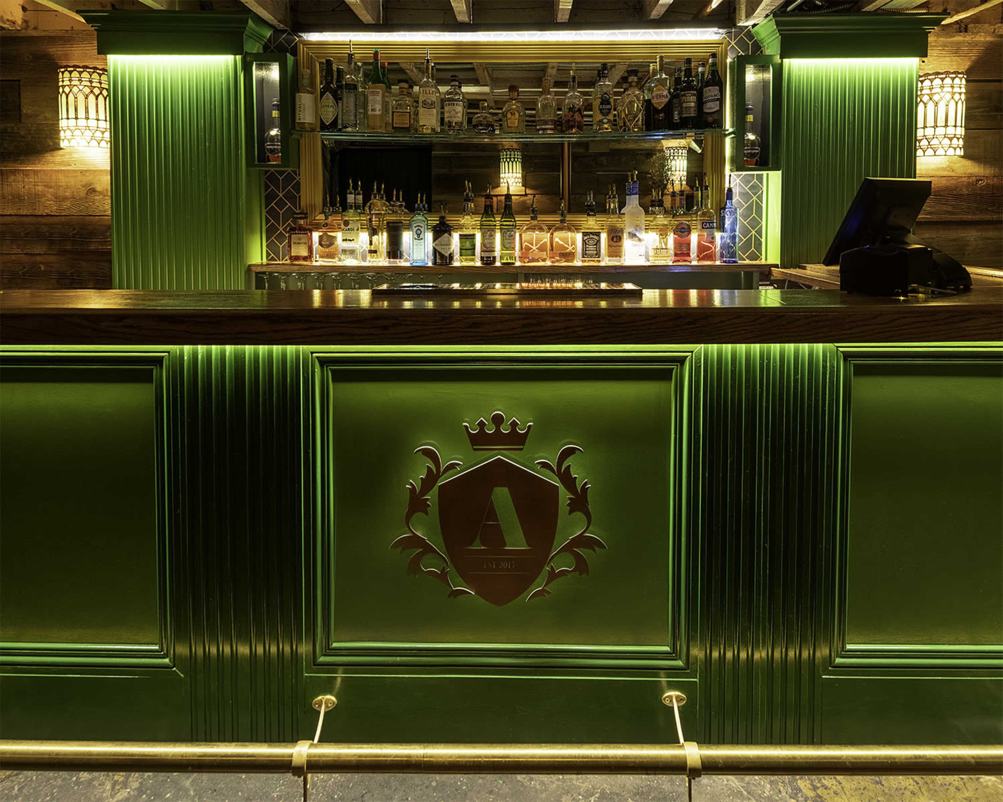 A stylish bar with a green illuminated countertop and a variety of liquor bottles displayed on shelves behind it.