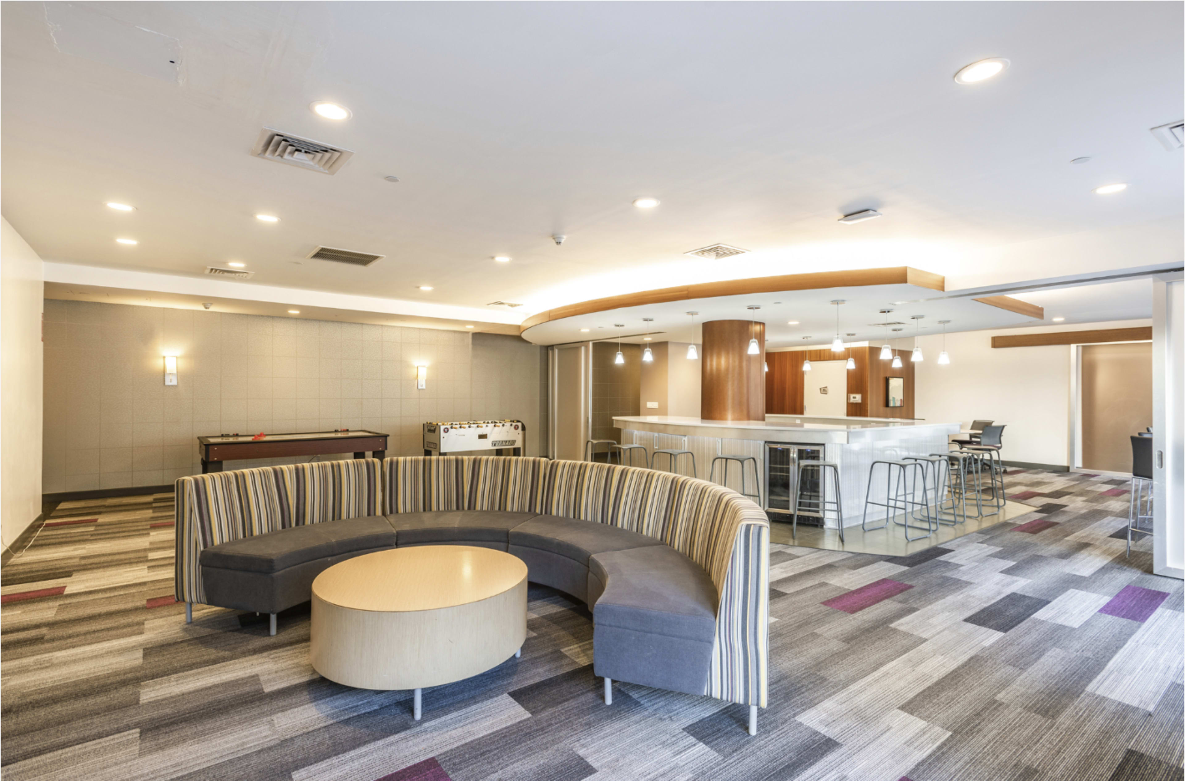 The image shows a modern lounge area featuring a curved seating arrangement, a pool table, and a bar counter set in a brightly lit space.