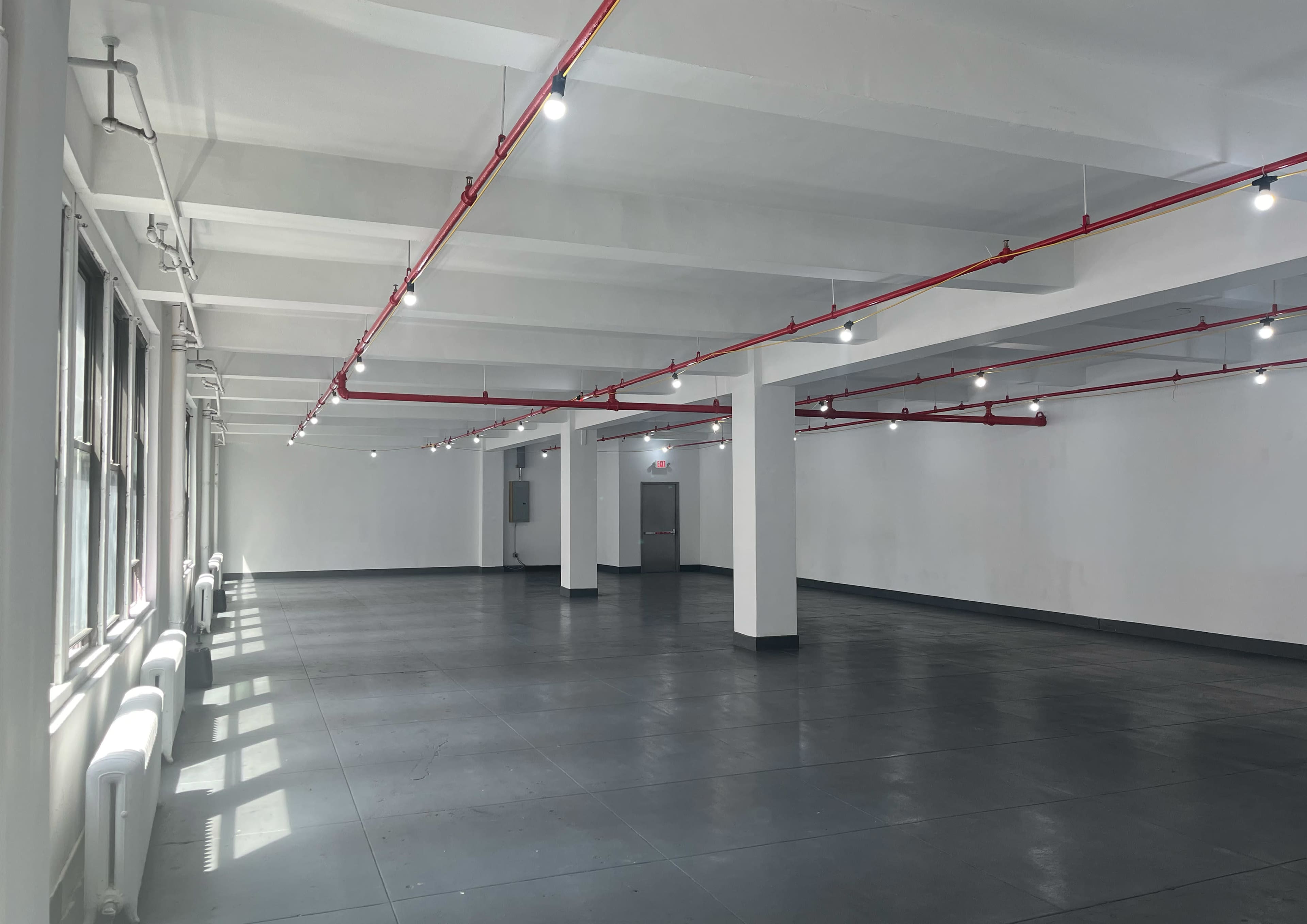 The image shows an empty, well-lit industrial space with polished concrete flooring and exposed piping along the ceiling.