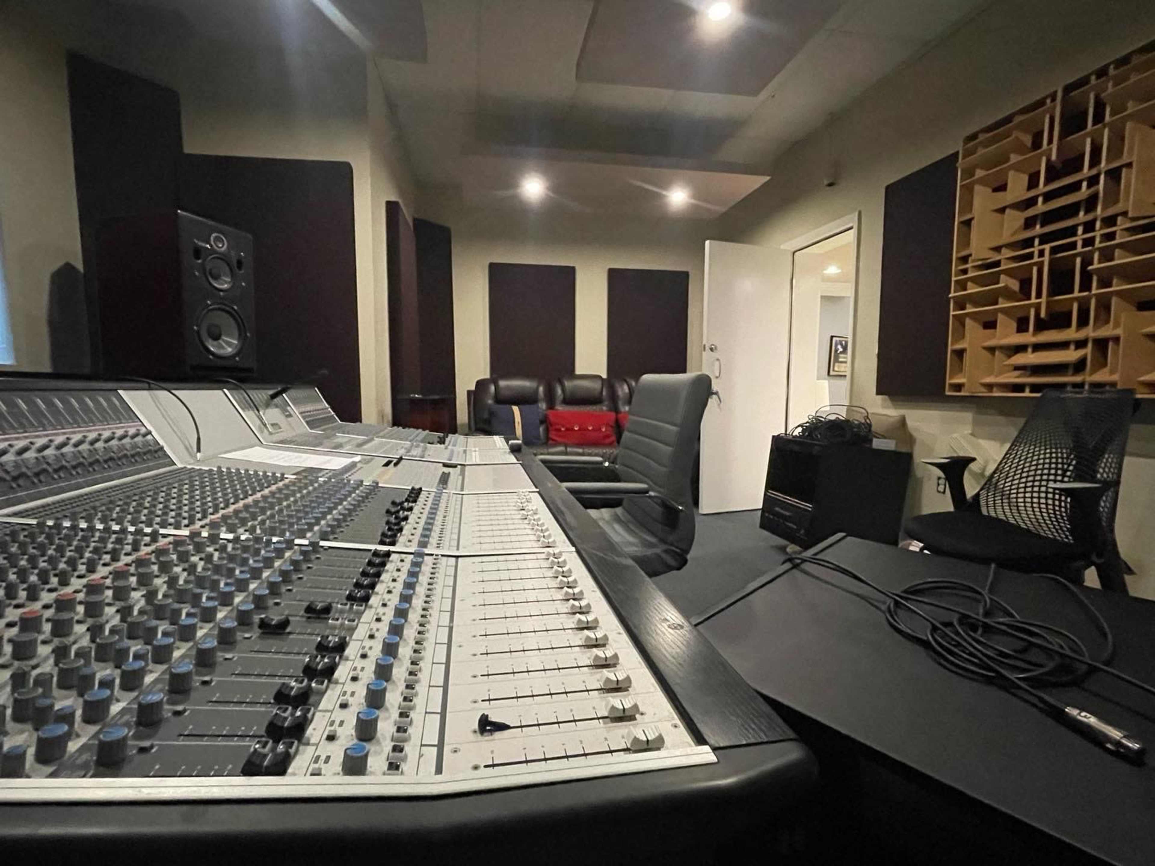 The image shows a recording studio with a large mixing console, an empty chair, and soundproofed walls.