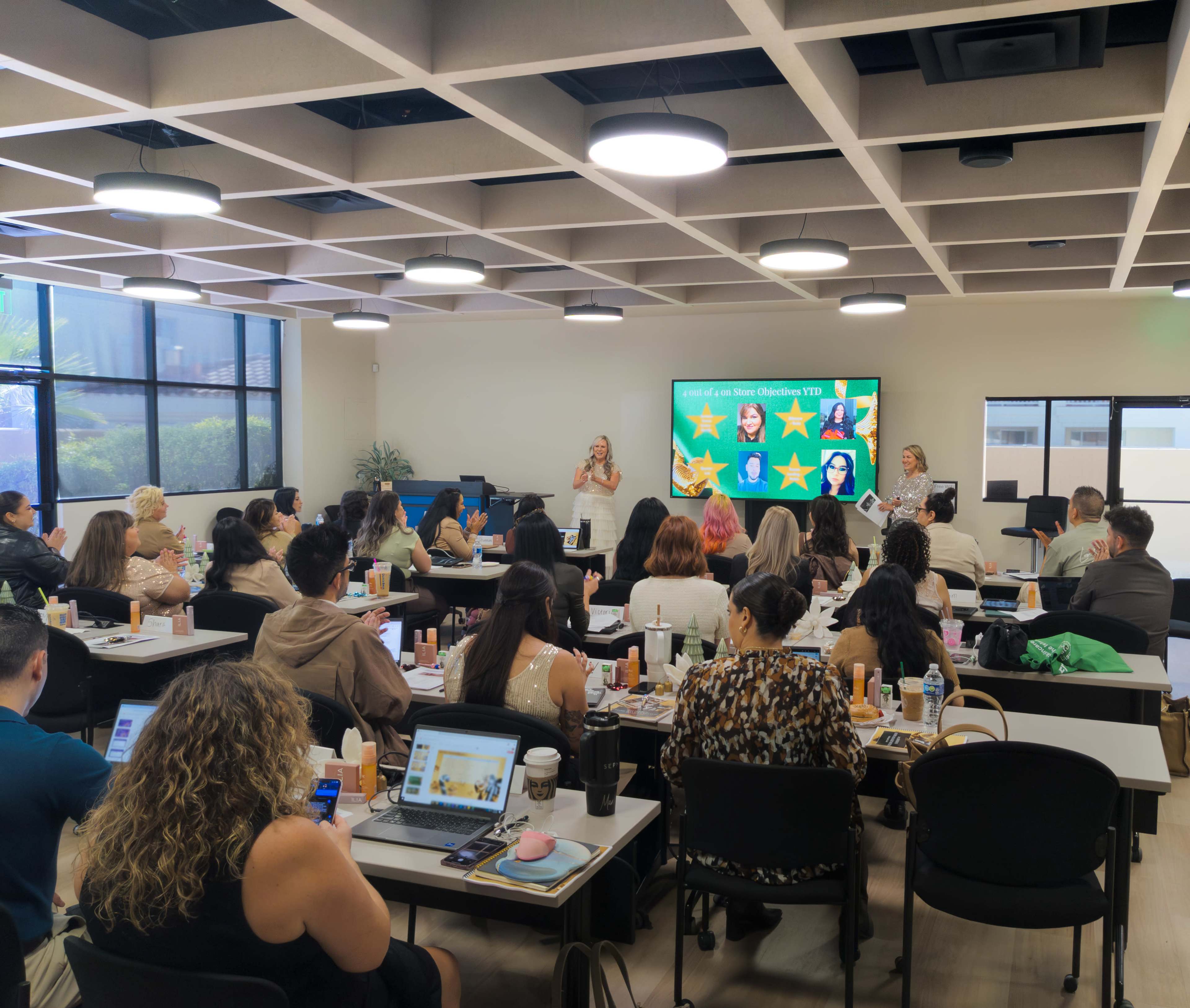 A group of people is seated in a modern conference room, attentively watching a presentation on a screen at the front.