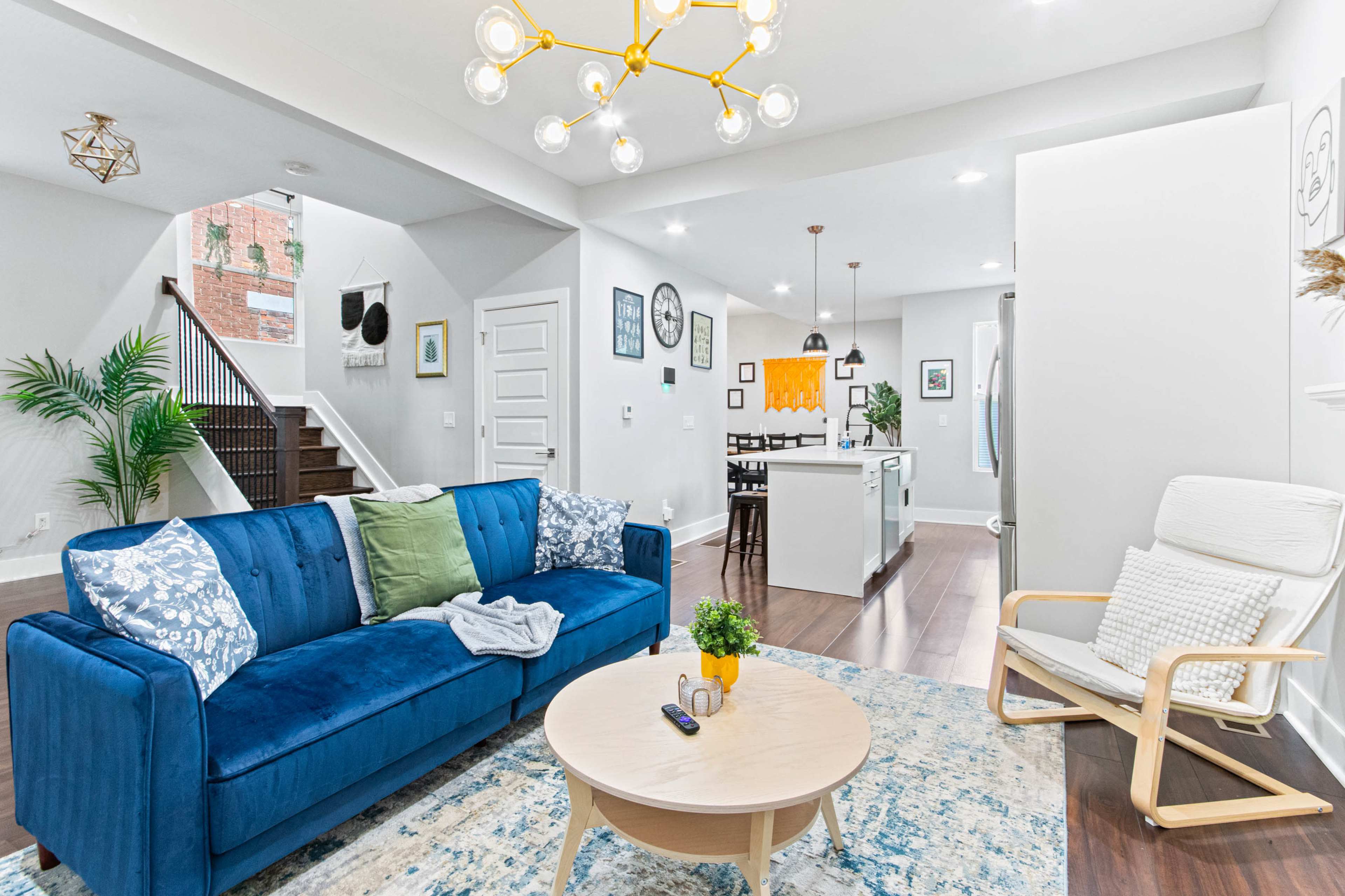 A modern living room features a blue sofa, a round coffee table, and an adjacent open kitchen with dining space.