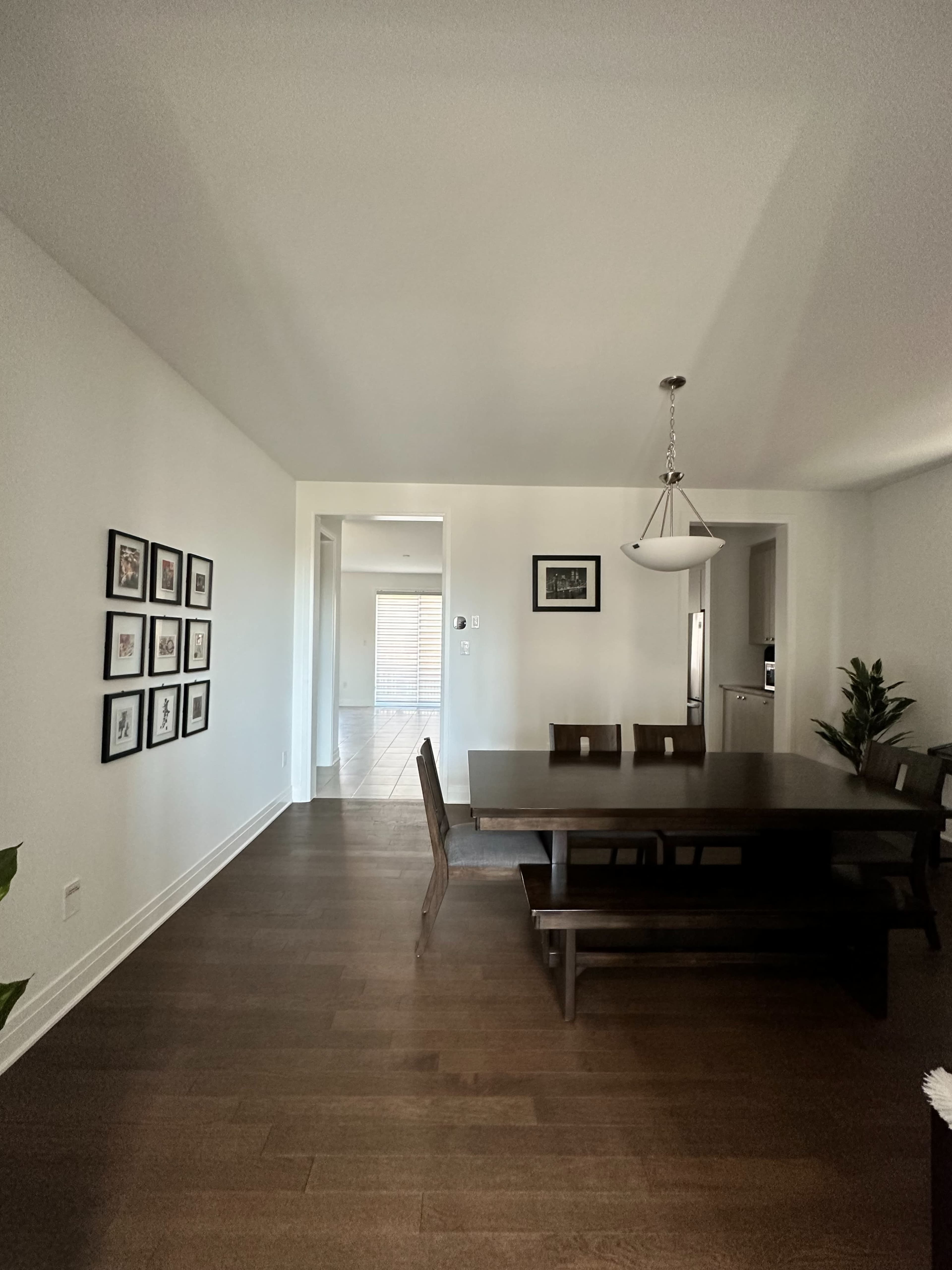 A dining area with a dark wooden table surrounded by chairs, framed photographs on the wall, and an entryway leading to a kitchen in the background.