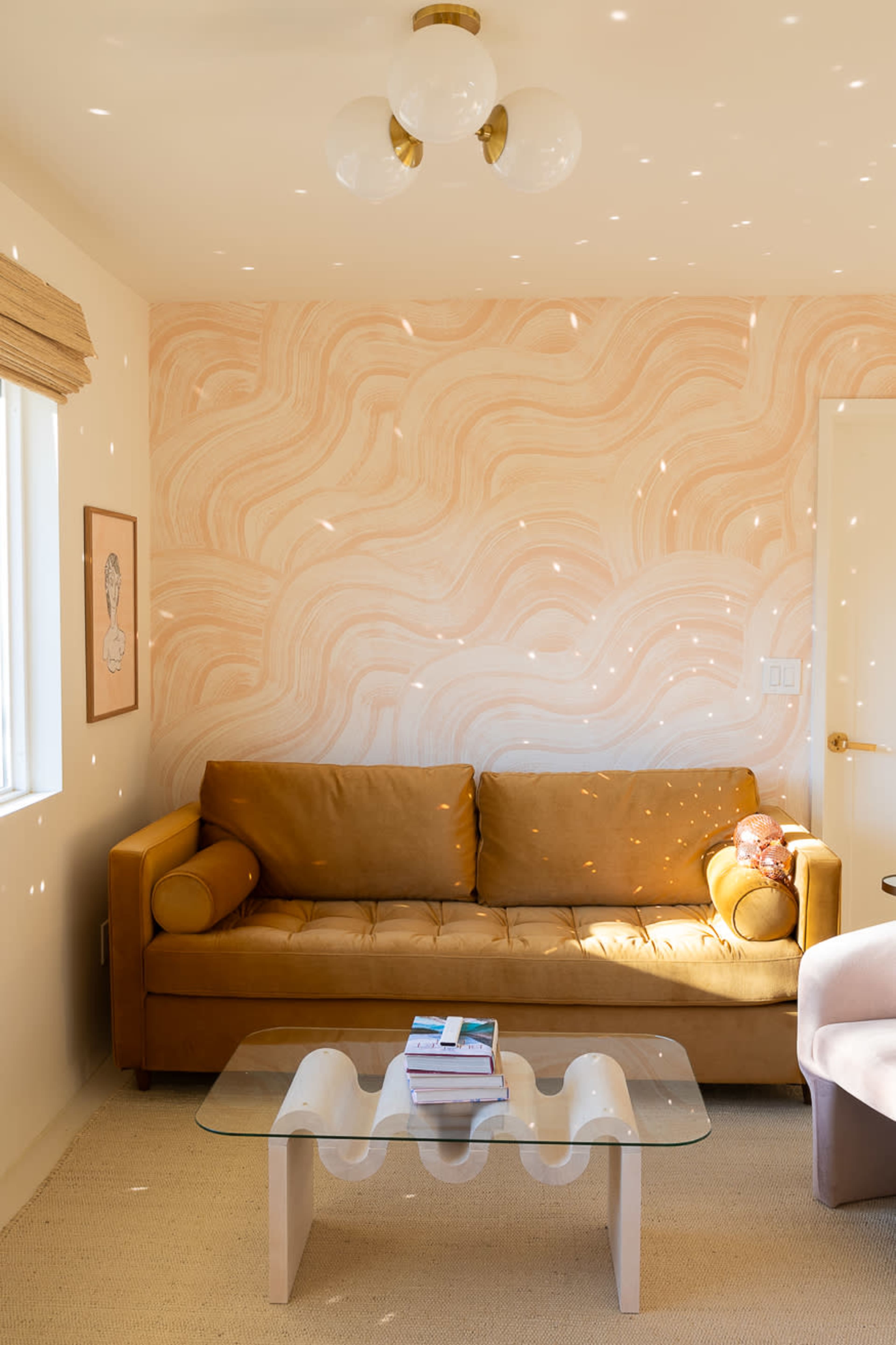 A cozy living room features a brown sofa, a glass coffee table, and a textured pink wall with decorative highlights.