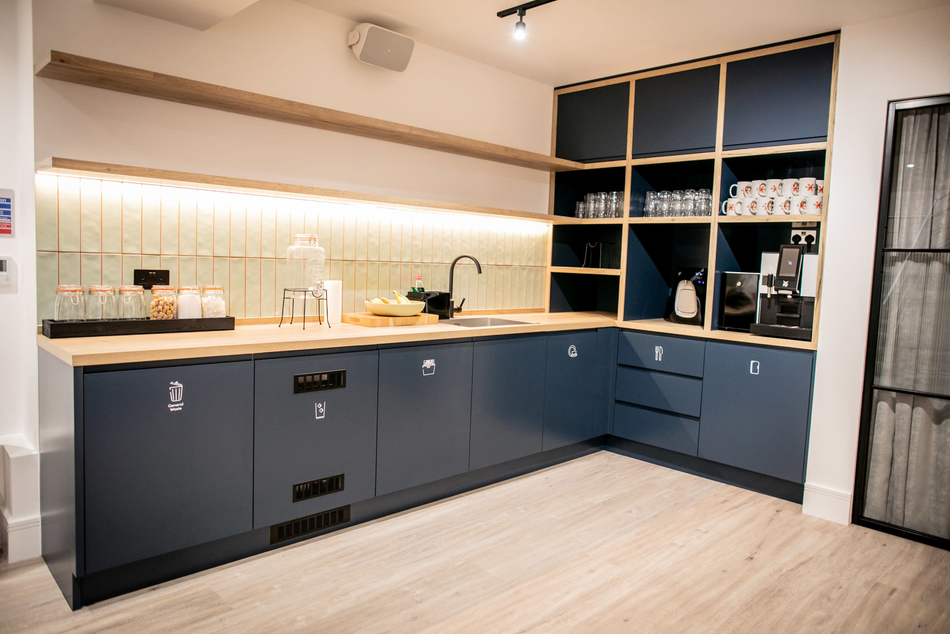 A modern kitchen with blue cabinetry, a wooden countertop, and glassware displayed on shelves.