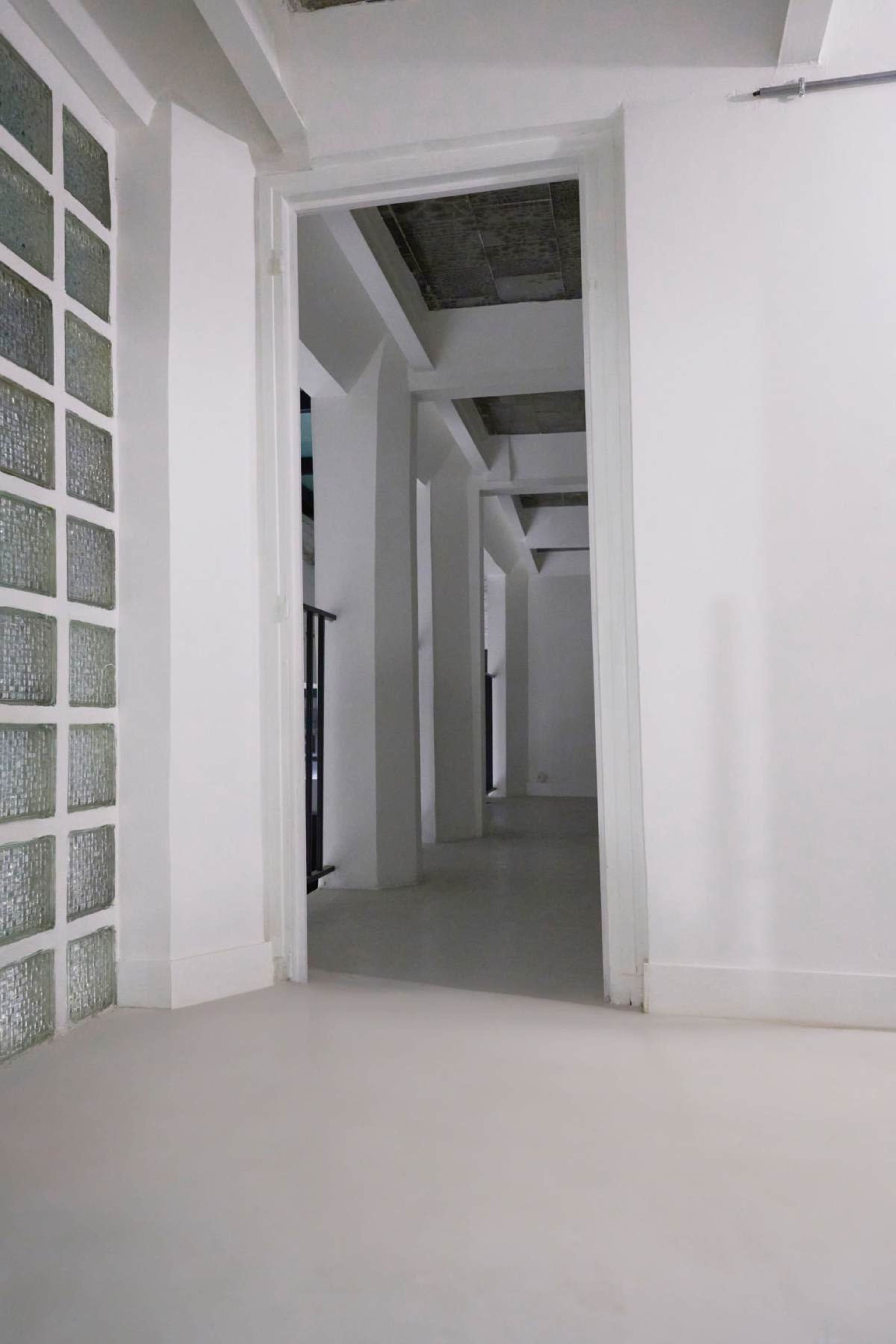 A spacious, minimalist interior features white walls and a light-colored floor, with a doorway leading to a hallway.