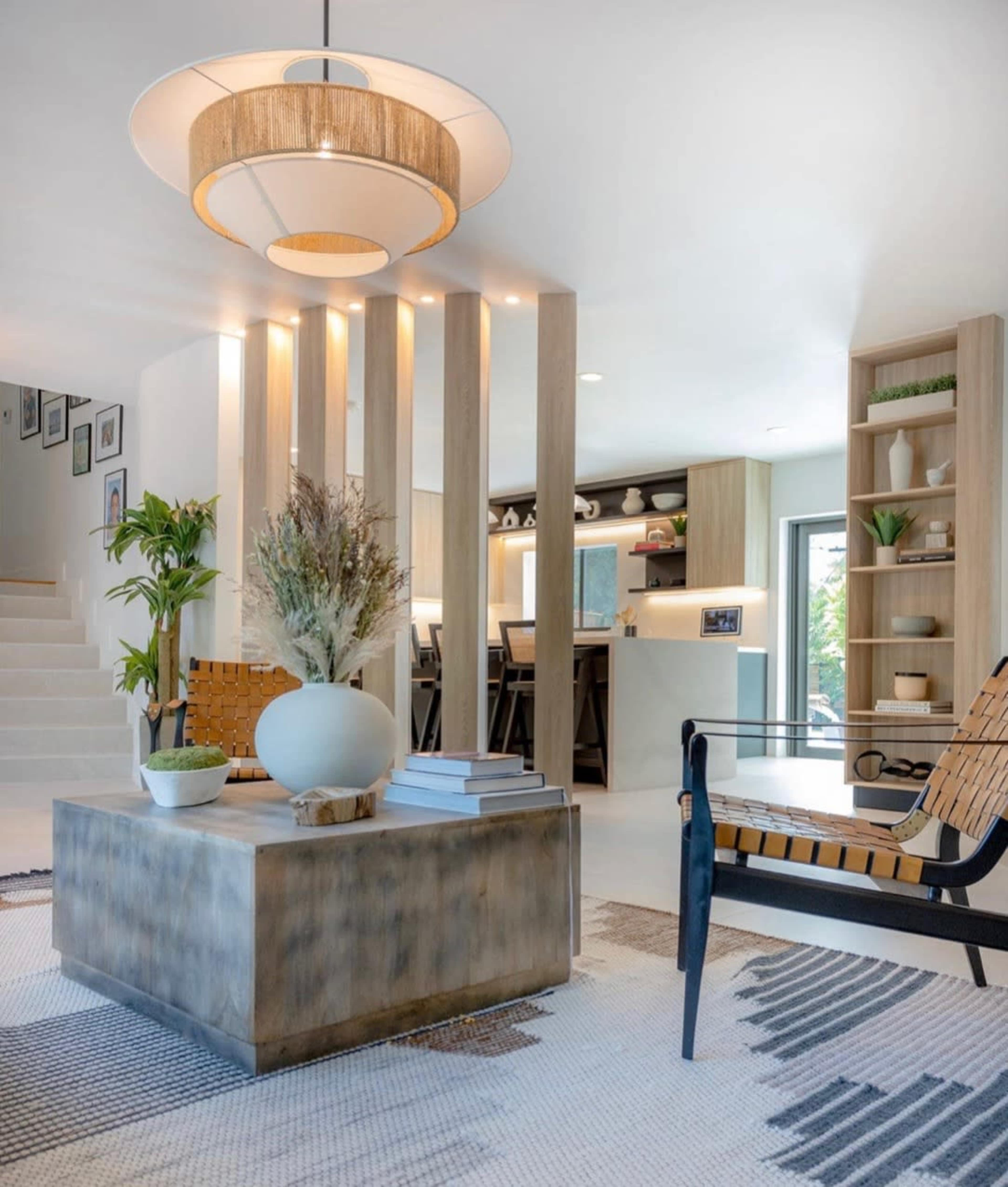 A modern living space with a central wooden coffee table, a patterned rug, and a large pendant light, surrounded by minimalist furniture and decor elements.