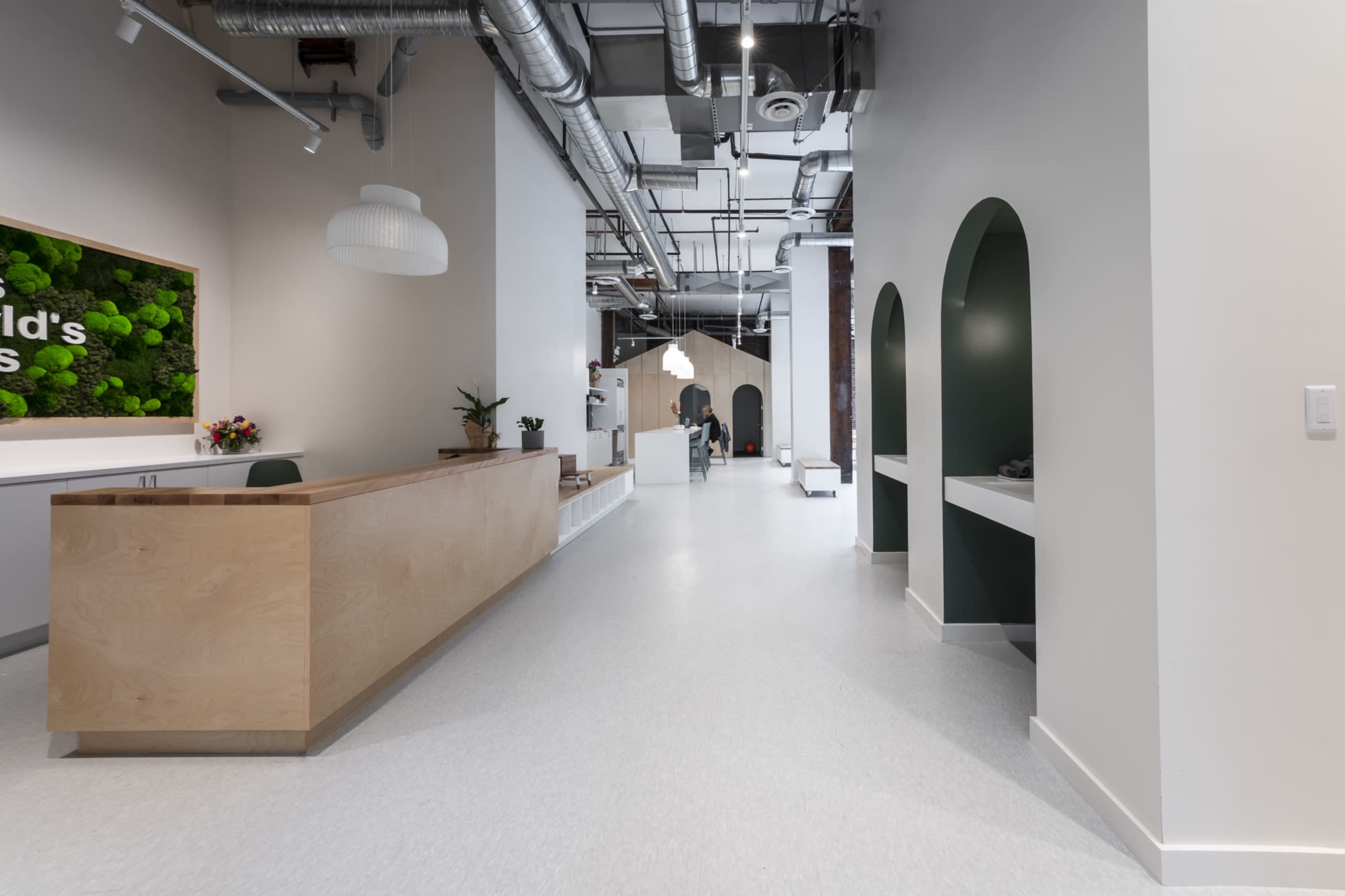 A modern reception area with a wooden front desk, green accents, and a spacious corridor leading to other rooms.