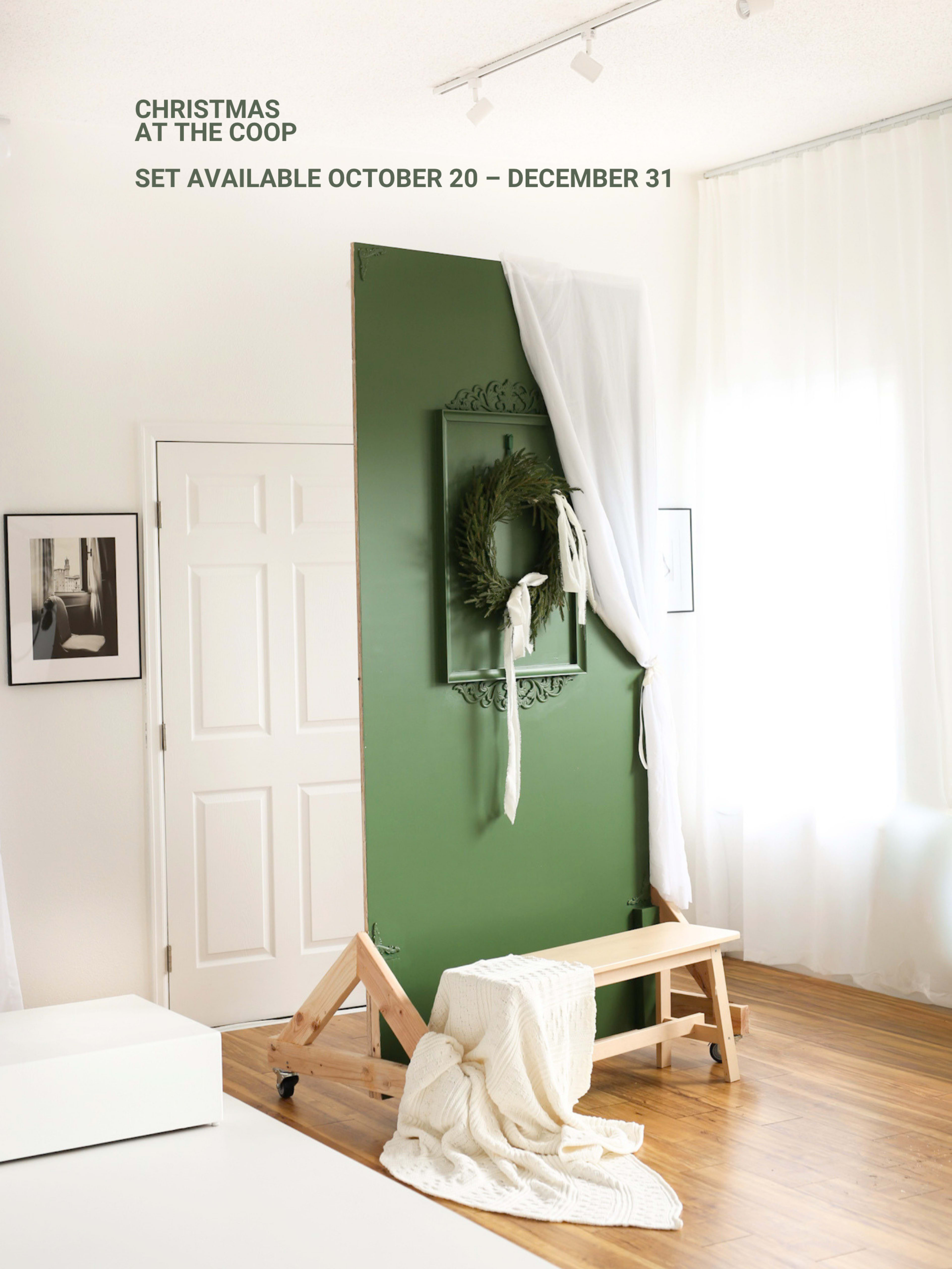 The image shows a green backdrop with a wreath, a bench in front, and white drapes, suggesting a holiday-themed photo setup.