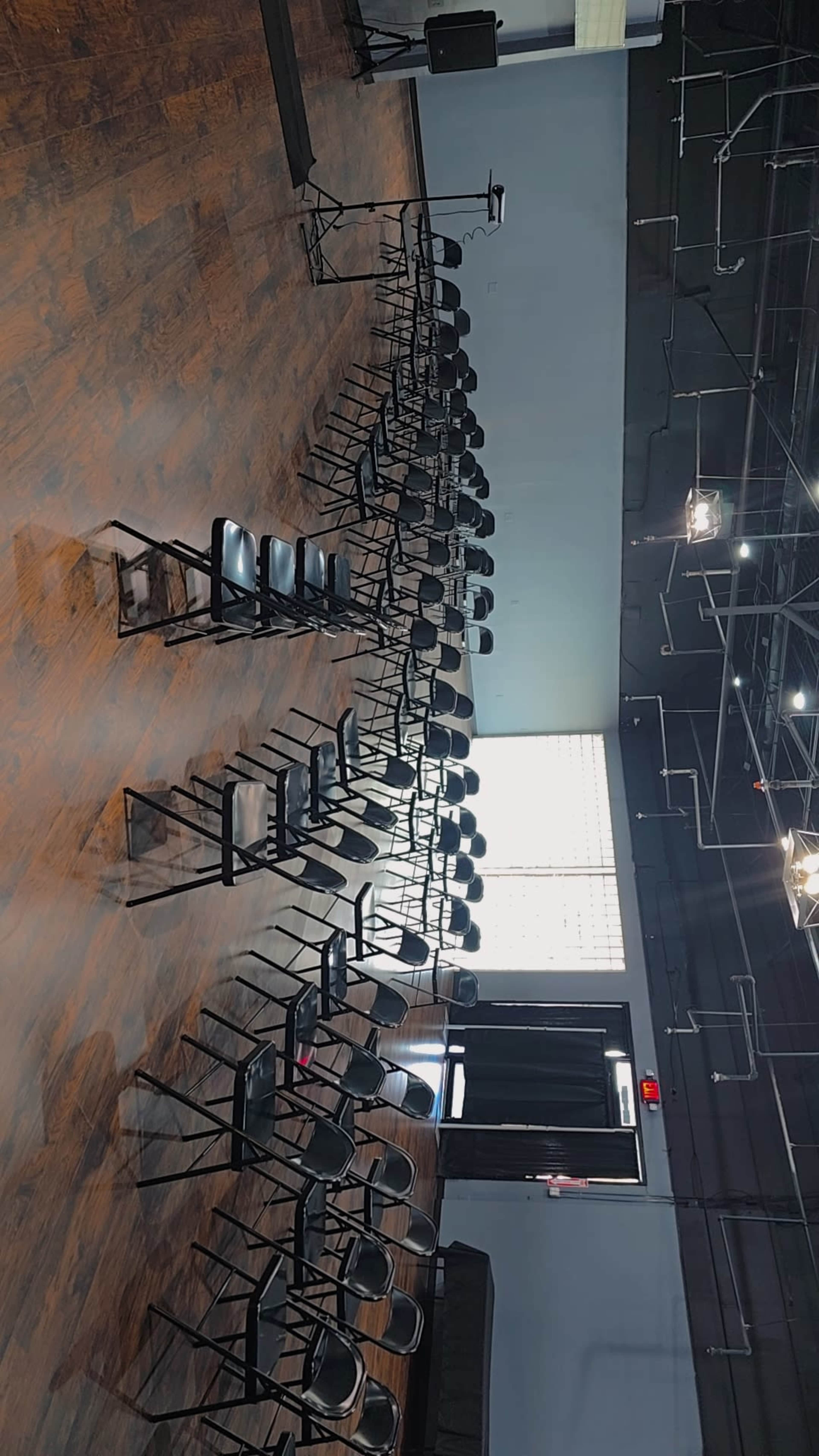 The image shows a room arranged with multiple rows of black chairs facing a stage or presentation area.