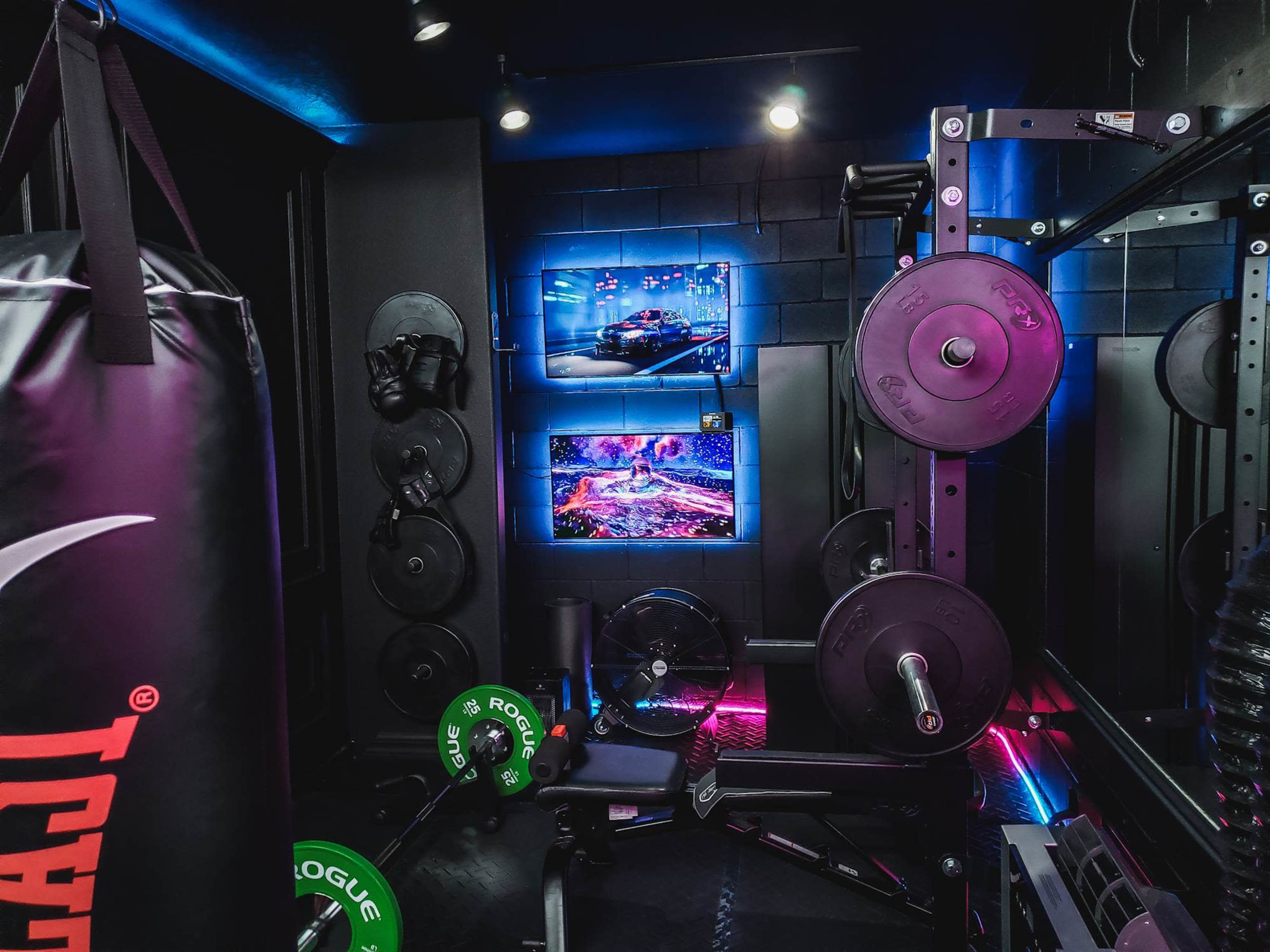 The image shows a gym space featuring a weightlifting setup, a punching bag, and a TV screen displaying vibrant visuals.