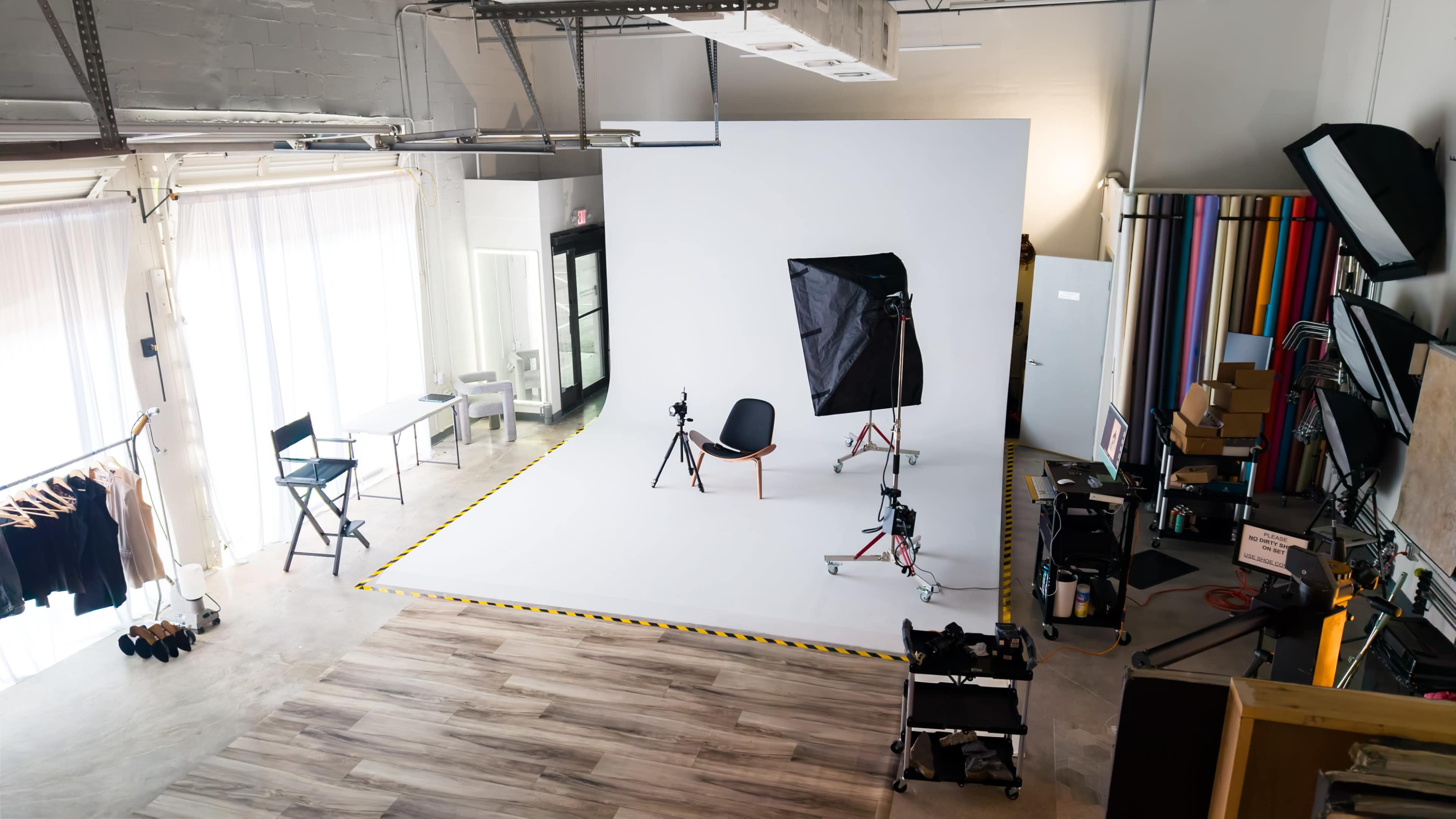 The image shows a spacious photo studio with a white backdrop, photography equipment, and various furnishings arranged around the area.