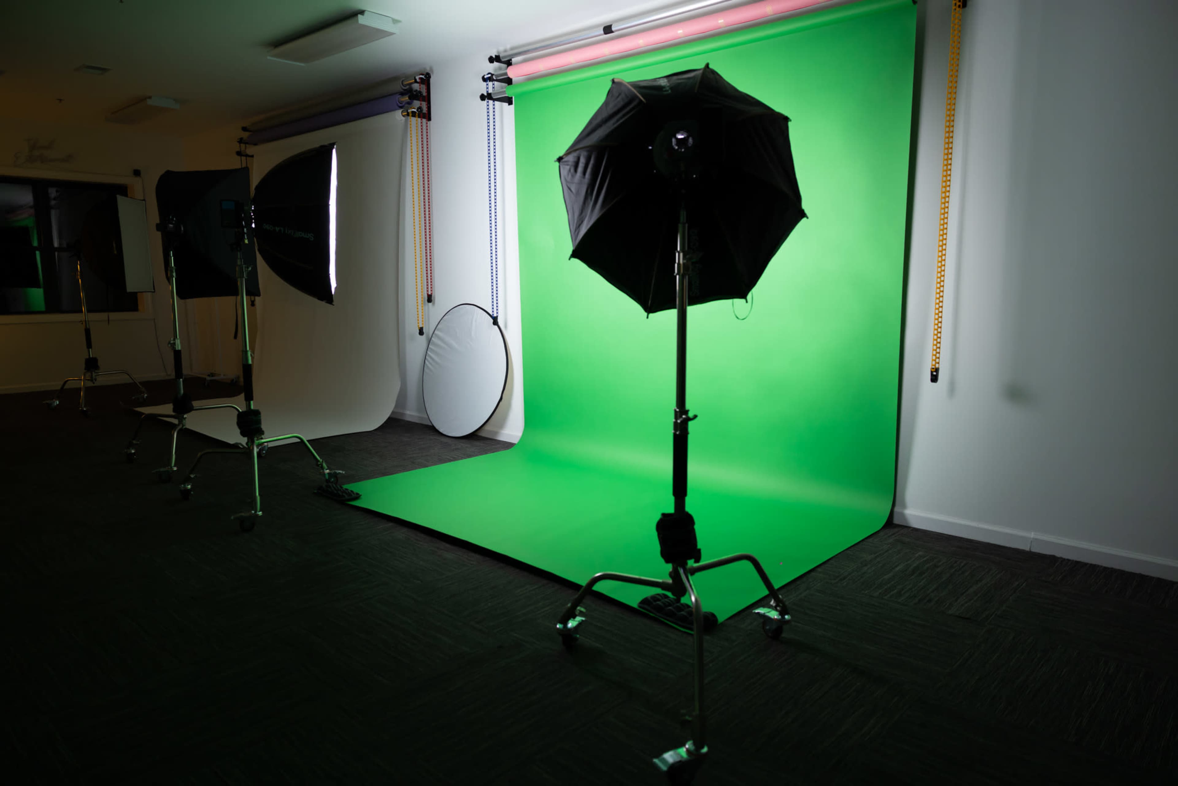 The image shows a photography studio with green and white backdrops, lighting equipment, and a circular reflector.
