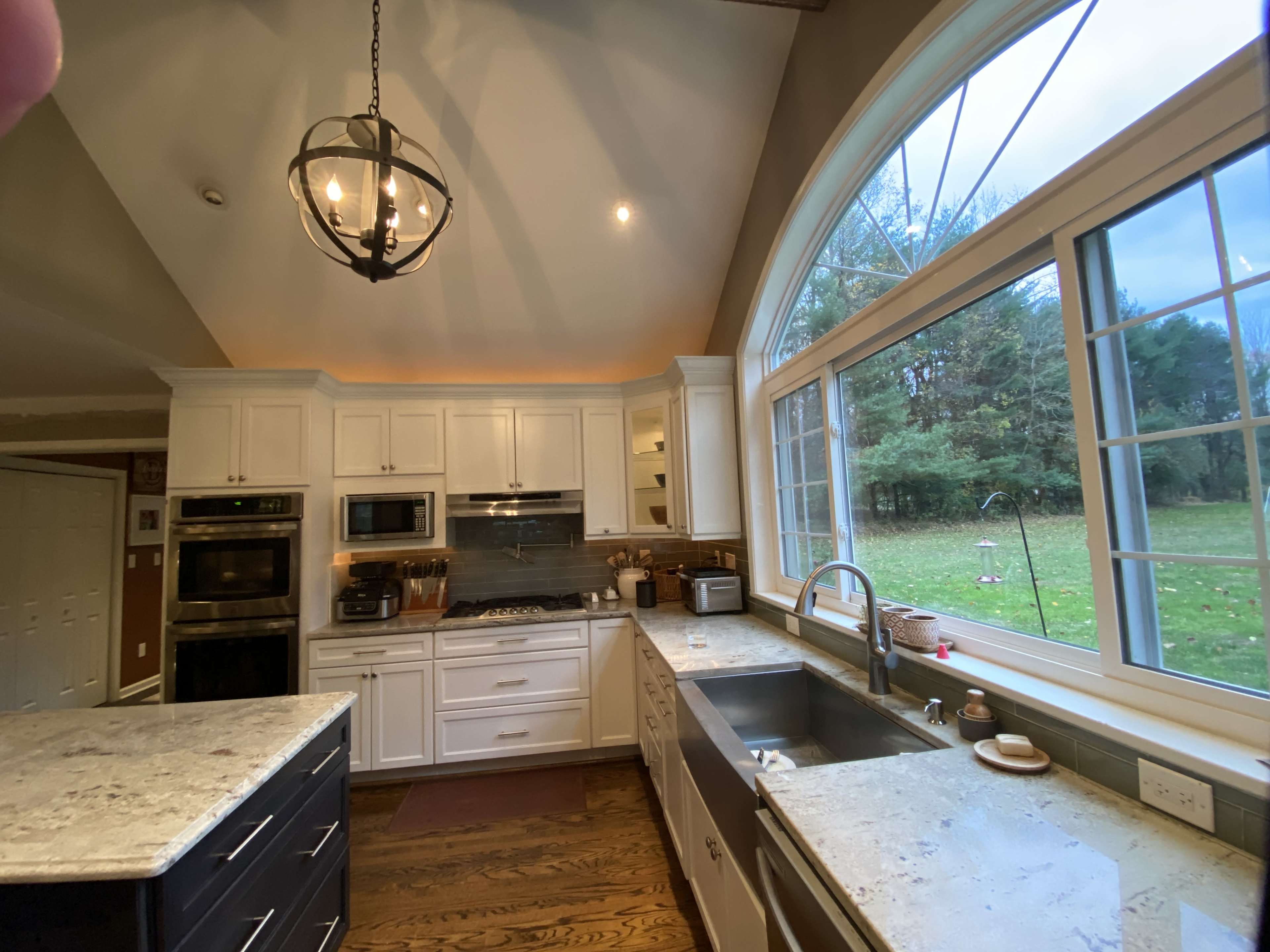 The kitchen features white cabinetry, stainless steel appliances, and a large window overlooking a green outdoor space.