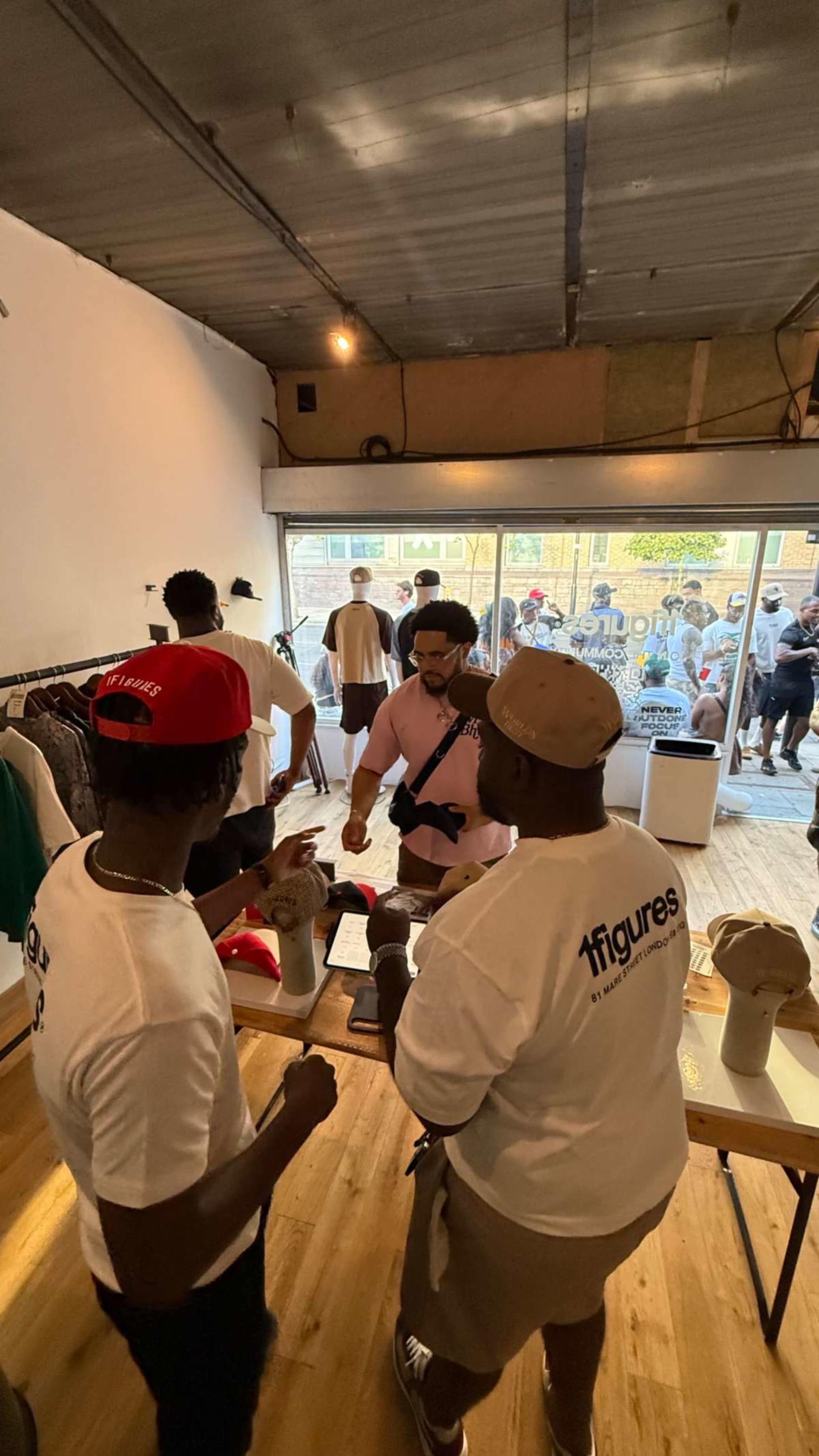 Two people in matching shirts assist a customer at a clothing store while a crowd is visible outside the large front window.