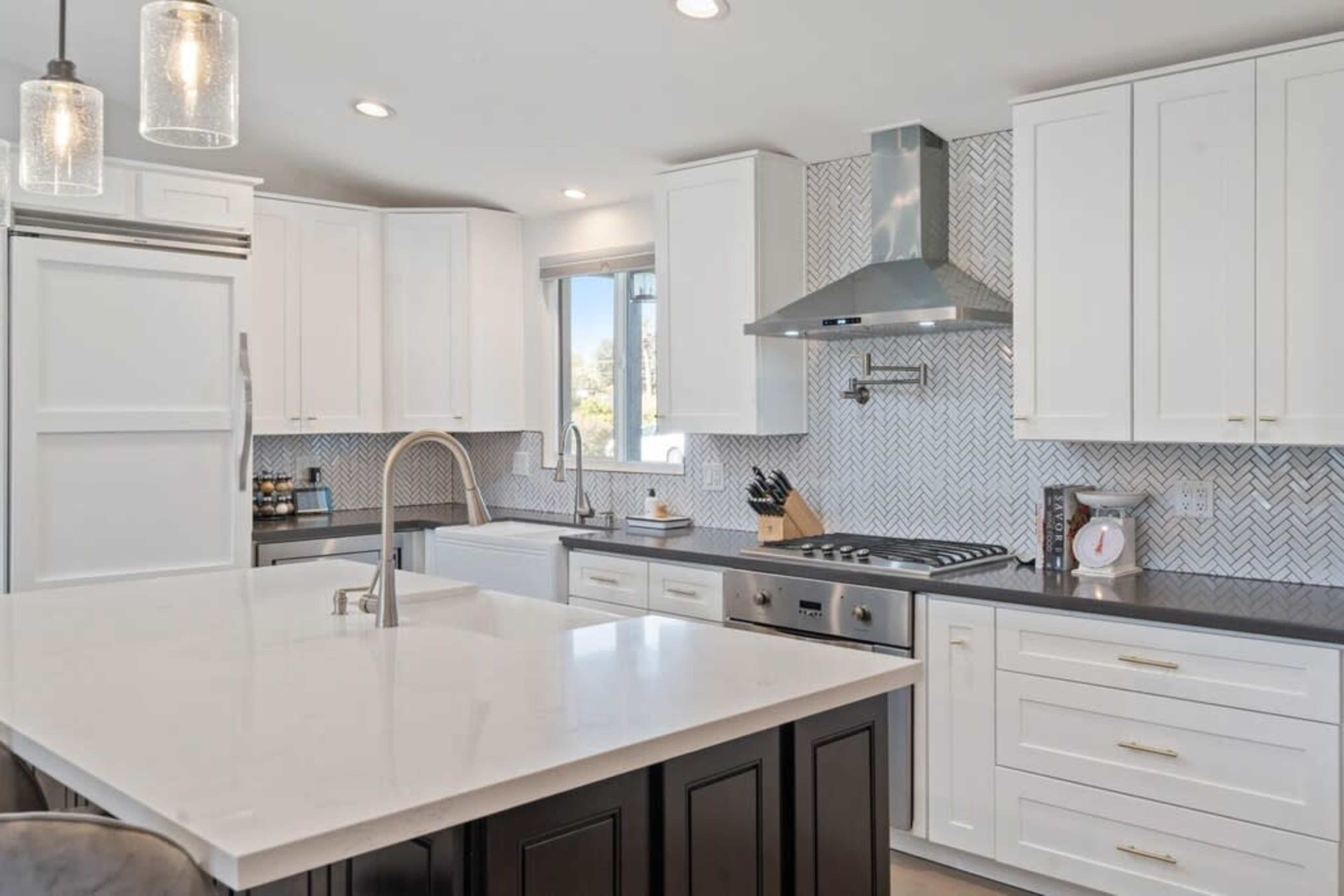 The kitchen features a central island with a white countertop, stainless steel appliances, and white cabinetry against a patterned backsplash.