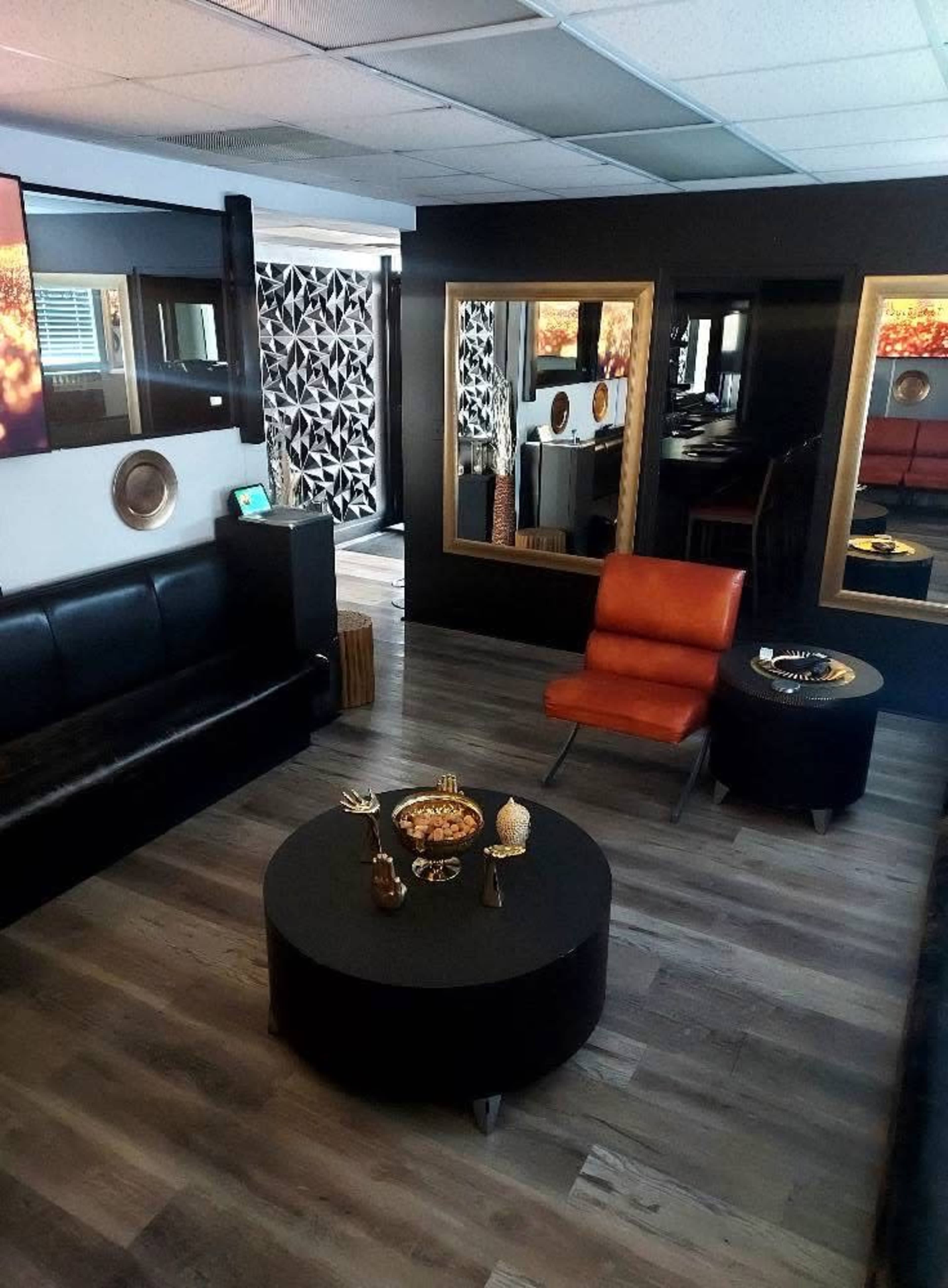 The image shows a modern lounge area with black furniture, a round coffee table, orange accent chair, and large mirrors on the walls.