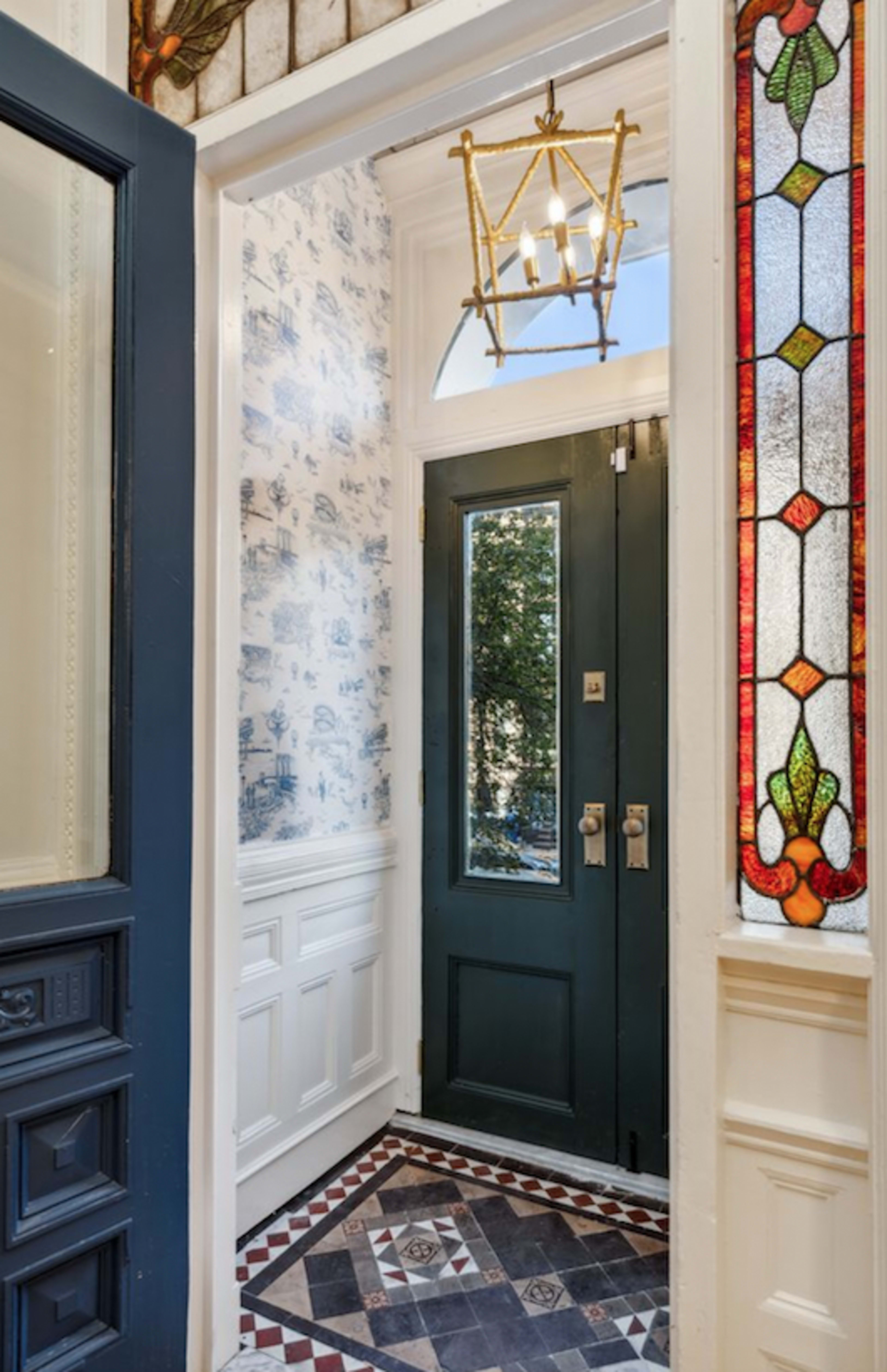 The image shows an entrance with a dark green door, a stained glass window, and intricate patterned tiles on the floor.